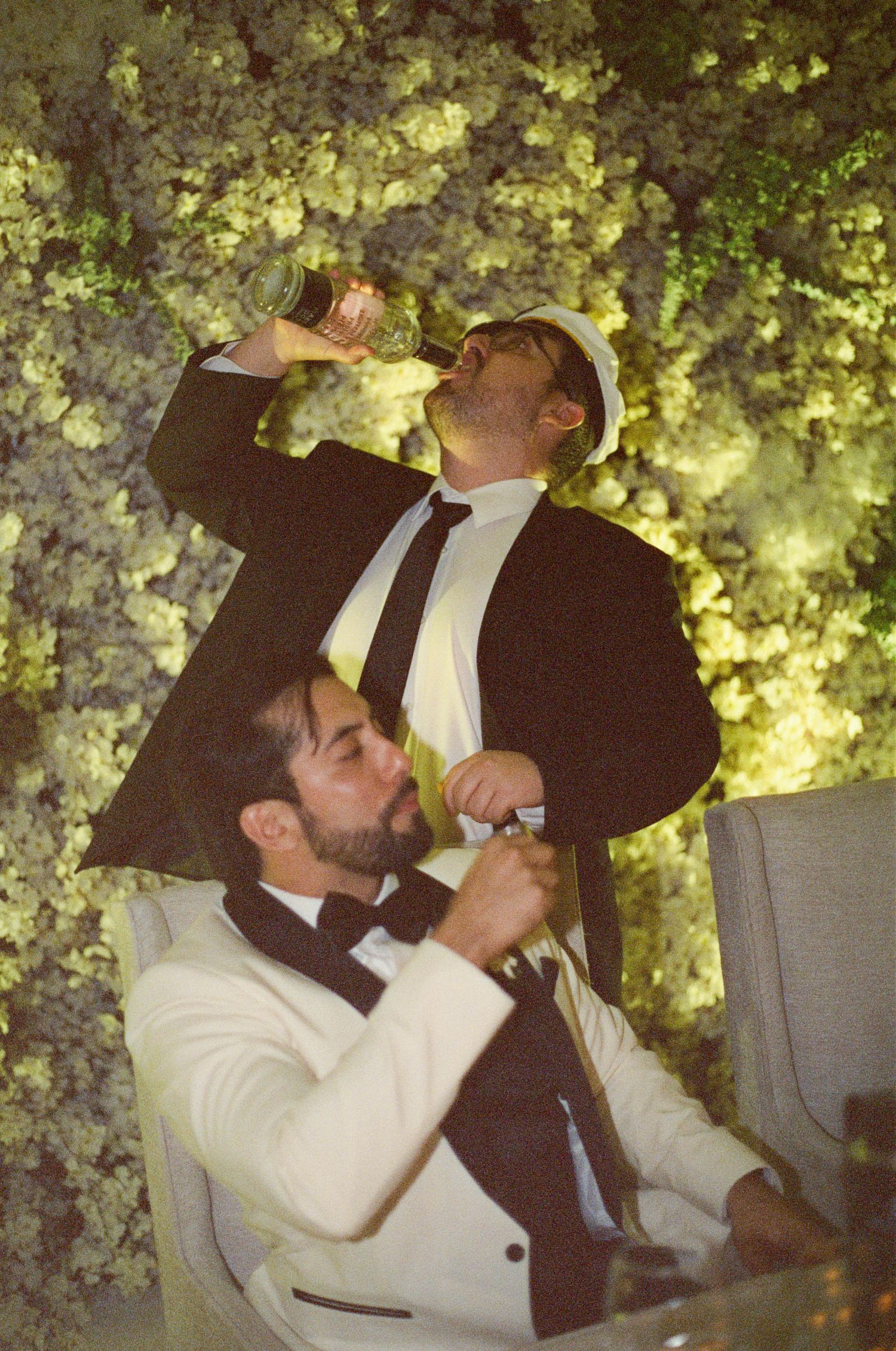 Guests at a wedding reception enjoy drinks together under outdoor lighting and foliage.