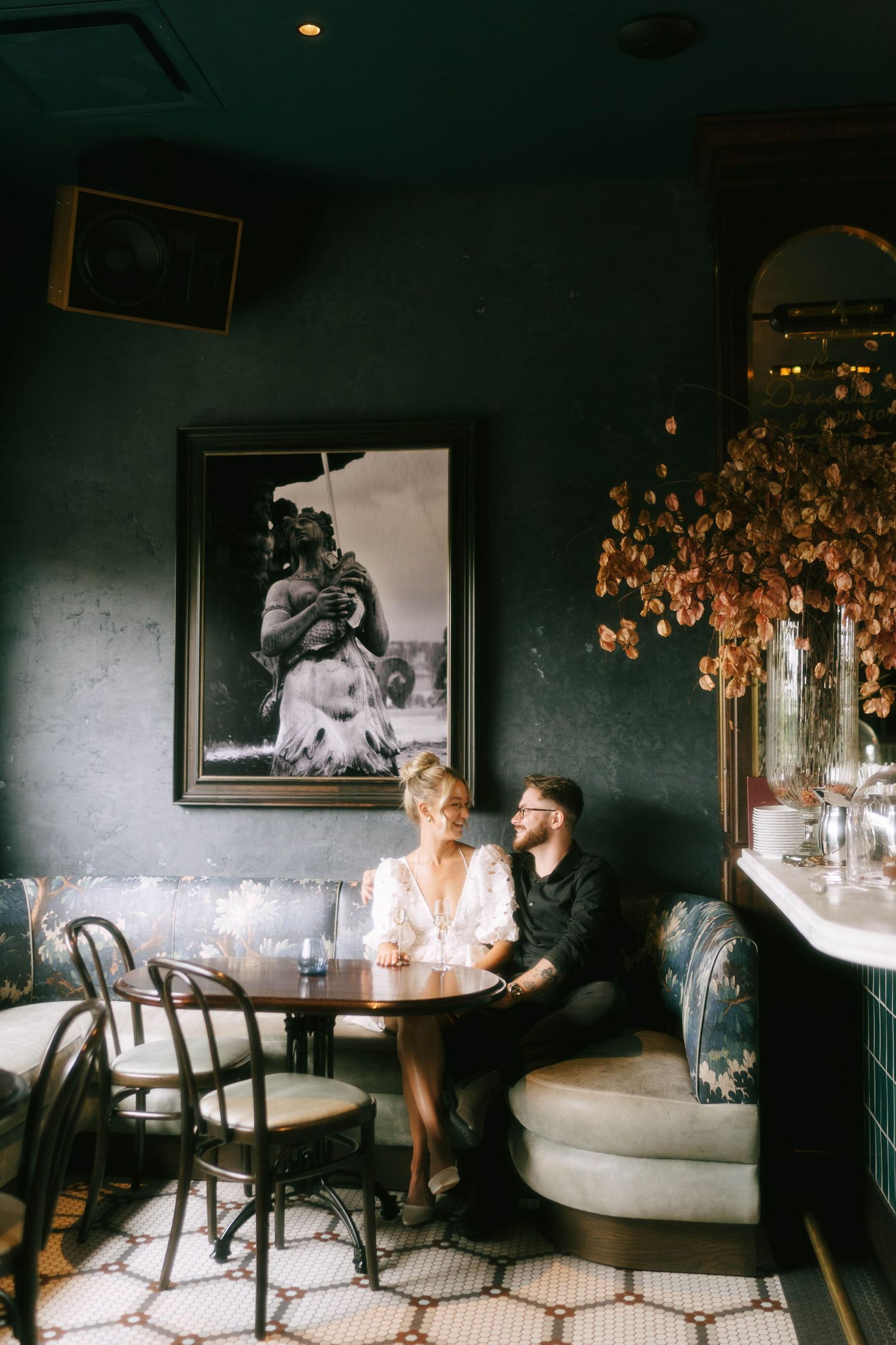 Couple sits together in a dimly lit restaurant booth with moody lighting and dark walls.