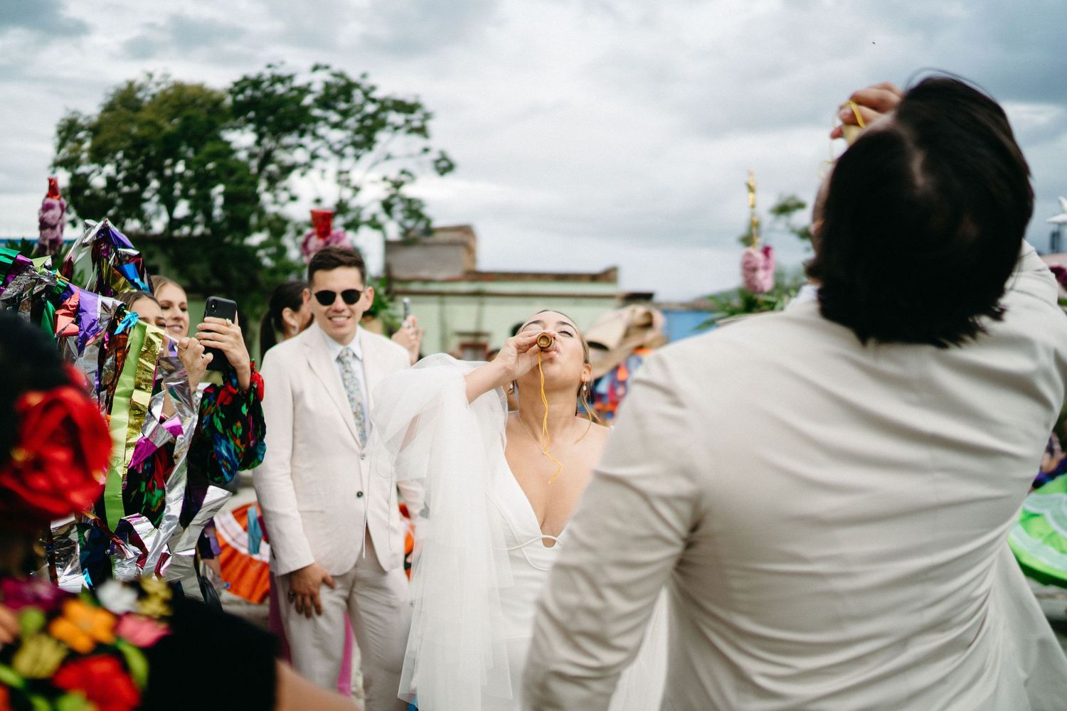 Outdoor wedding celebration with guests in bright colors against cloudy sky.