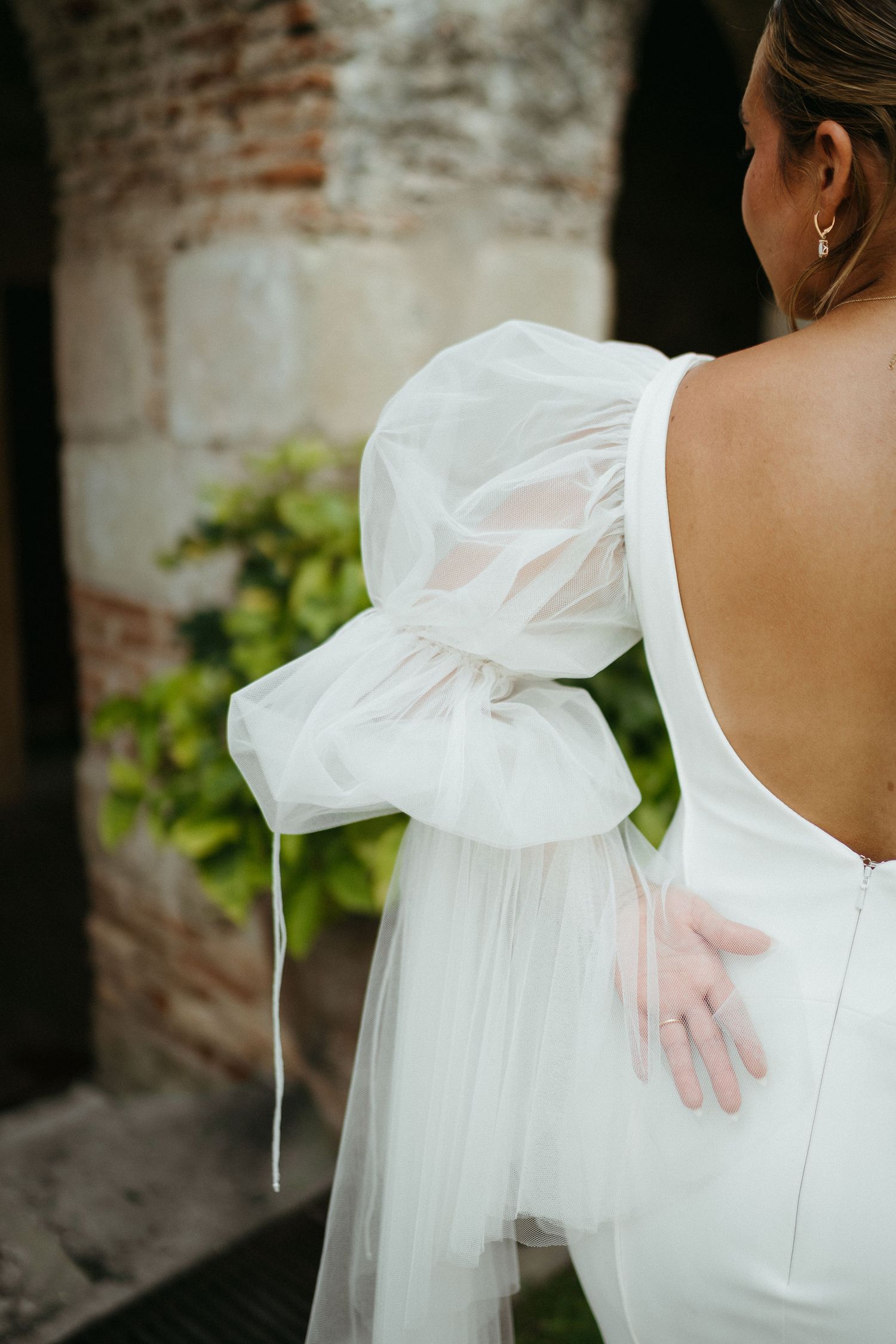 Close-up details of a white wedding dress bow and fabric against a brick wall background.