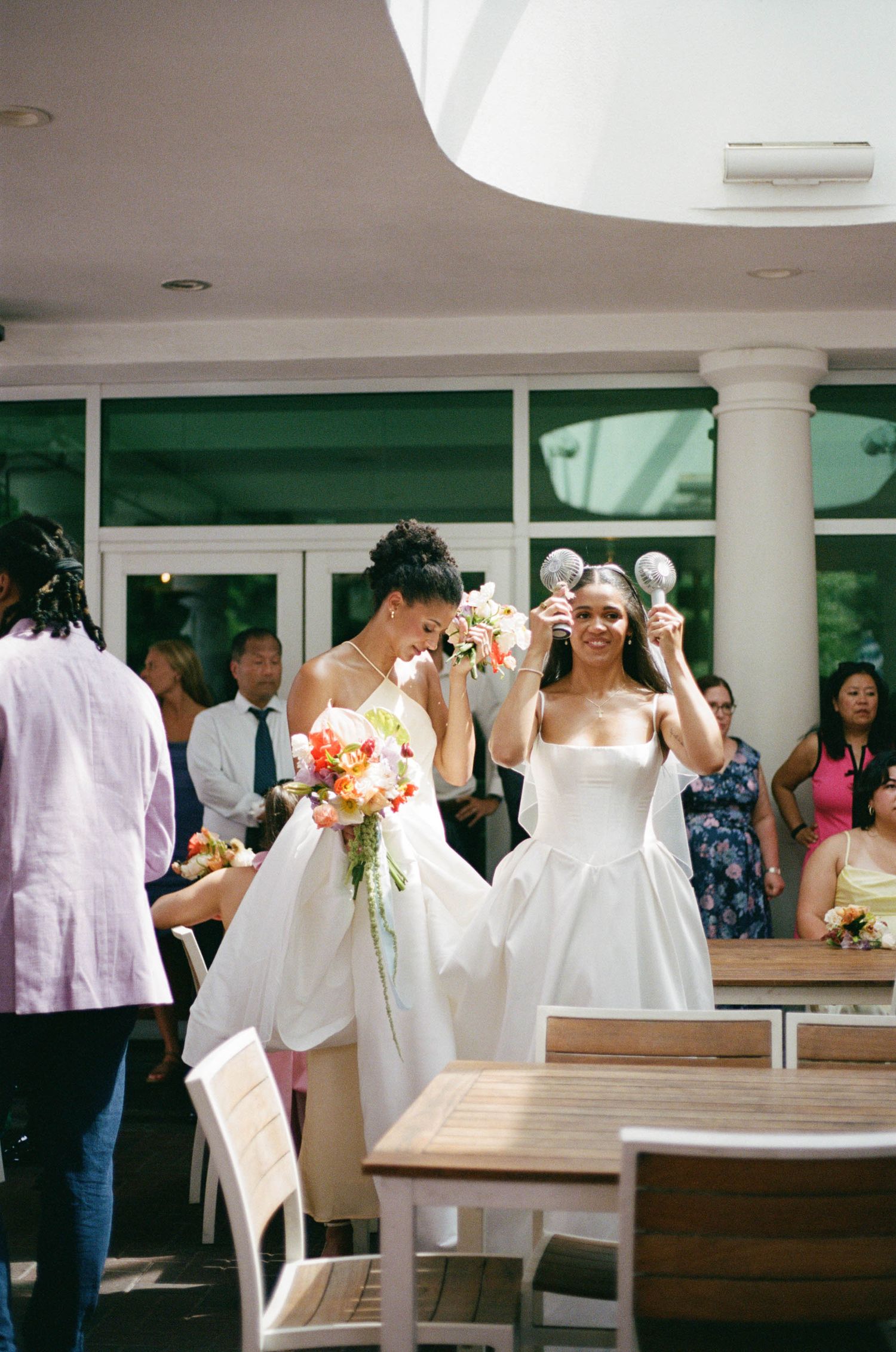 Wedding party gathering in a bright modern venue with white columns and decorative flowers.