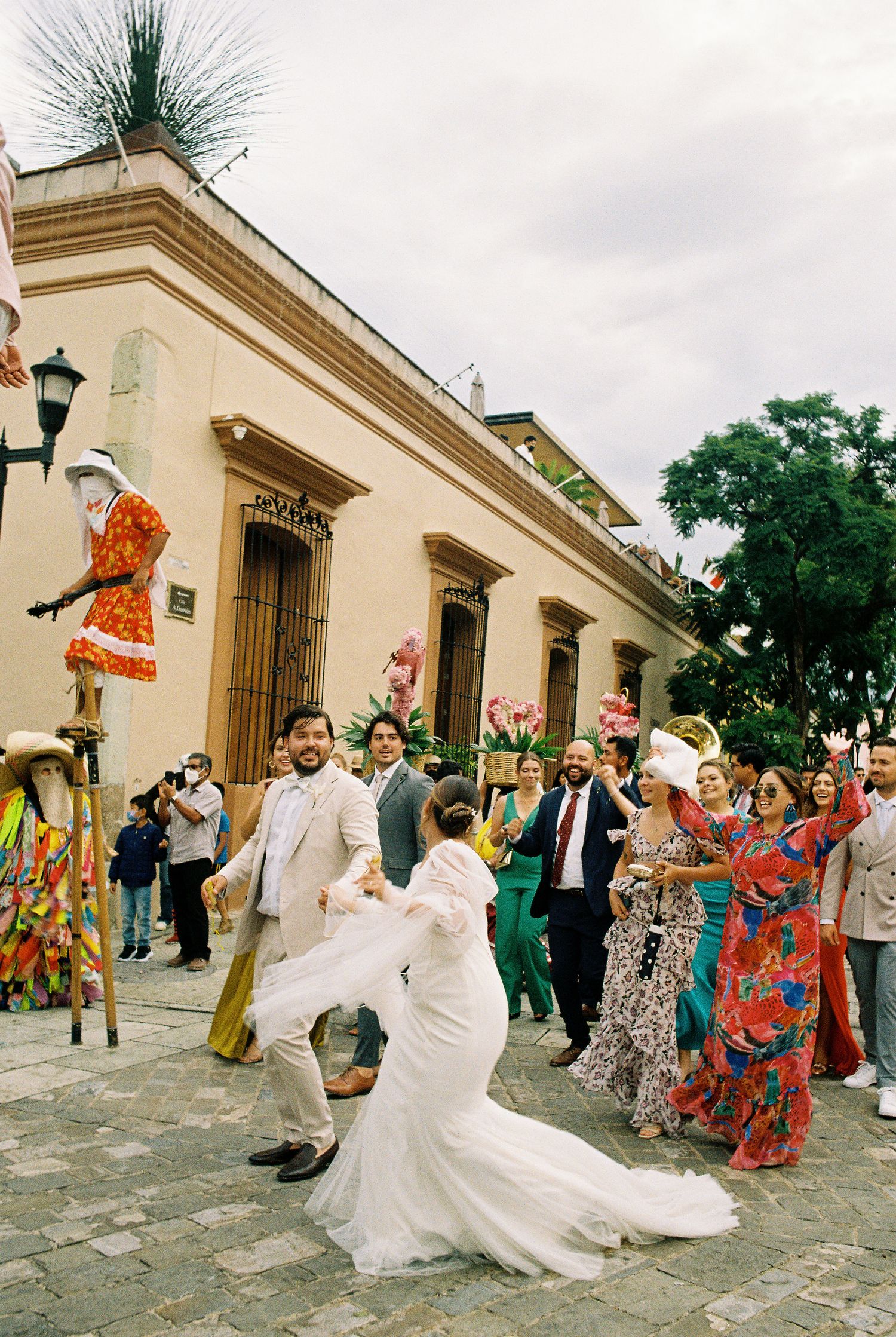 Wedding celebration in a colonial Mexican street with dancers in colorful traditional dresses and festive decorations.