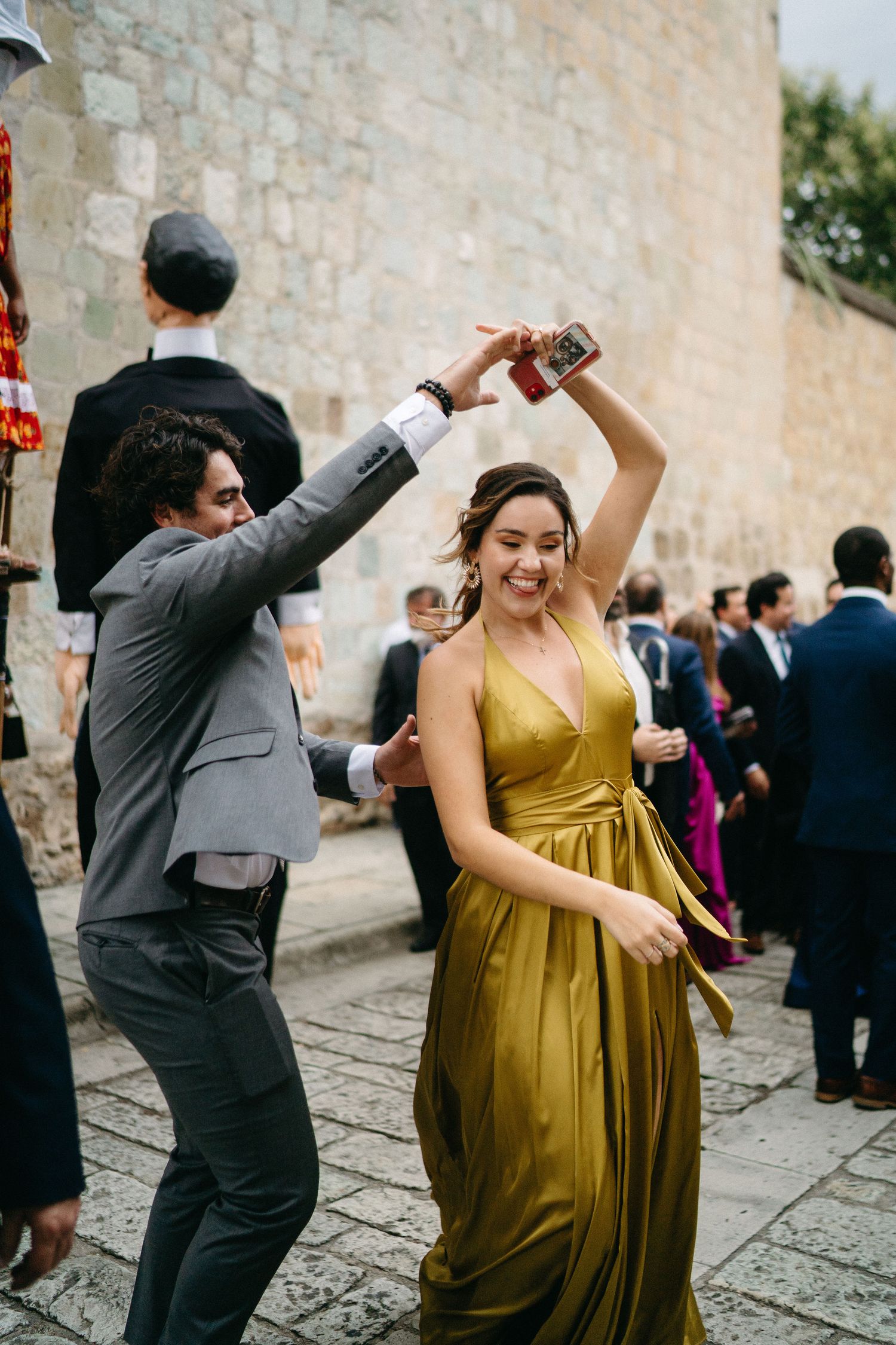 Wedding guests dance joyfully on cobblestone street in formal attire.