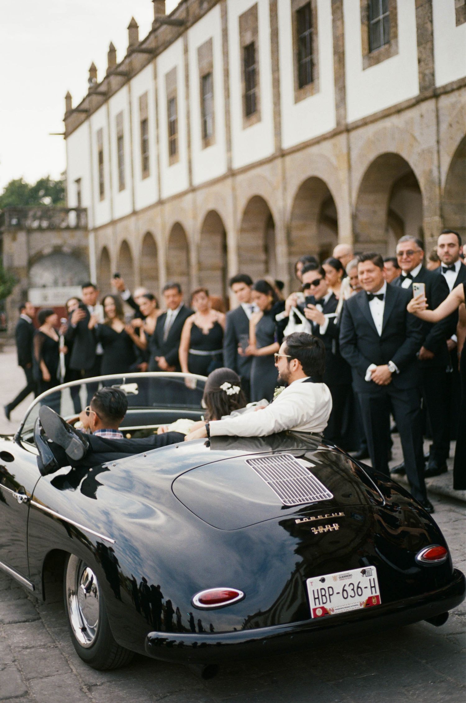 Classic black vintage car parked outside an elegant stone building with arched colonnade.