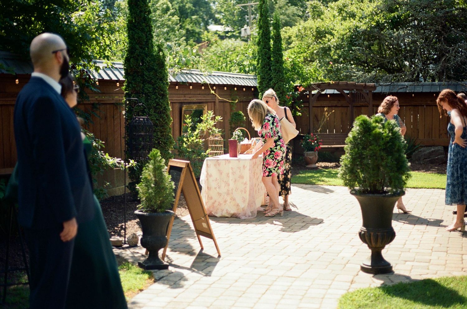 Garden party setup with guests mingling on a stone patio surrounded by greenery.