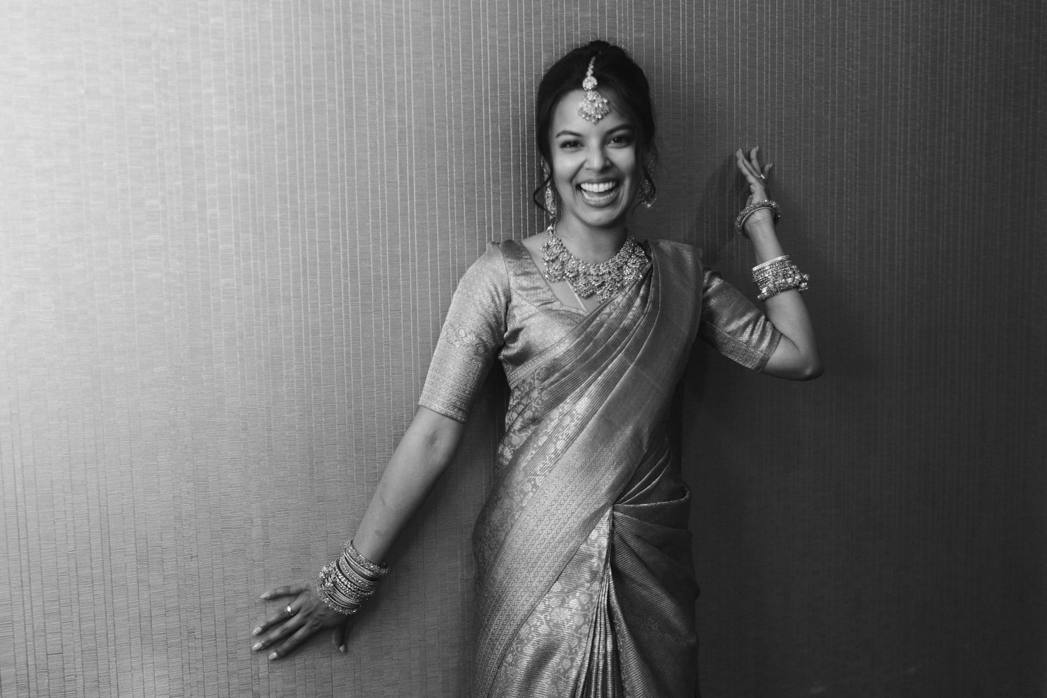 Black and white portrait of bride in traditional Indian saree with jewelry, smiling and posing gracefully.