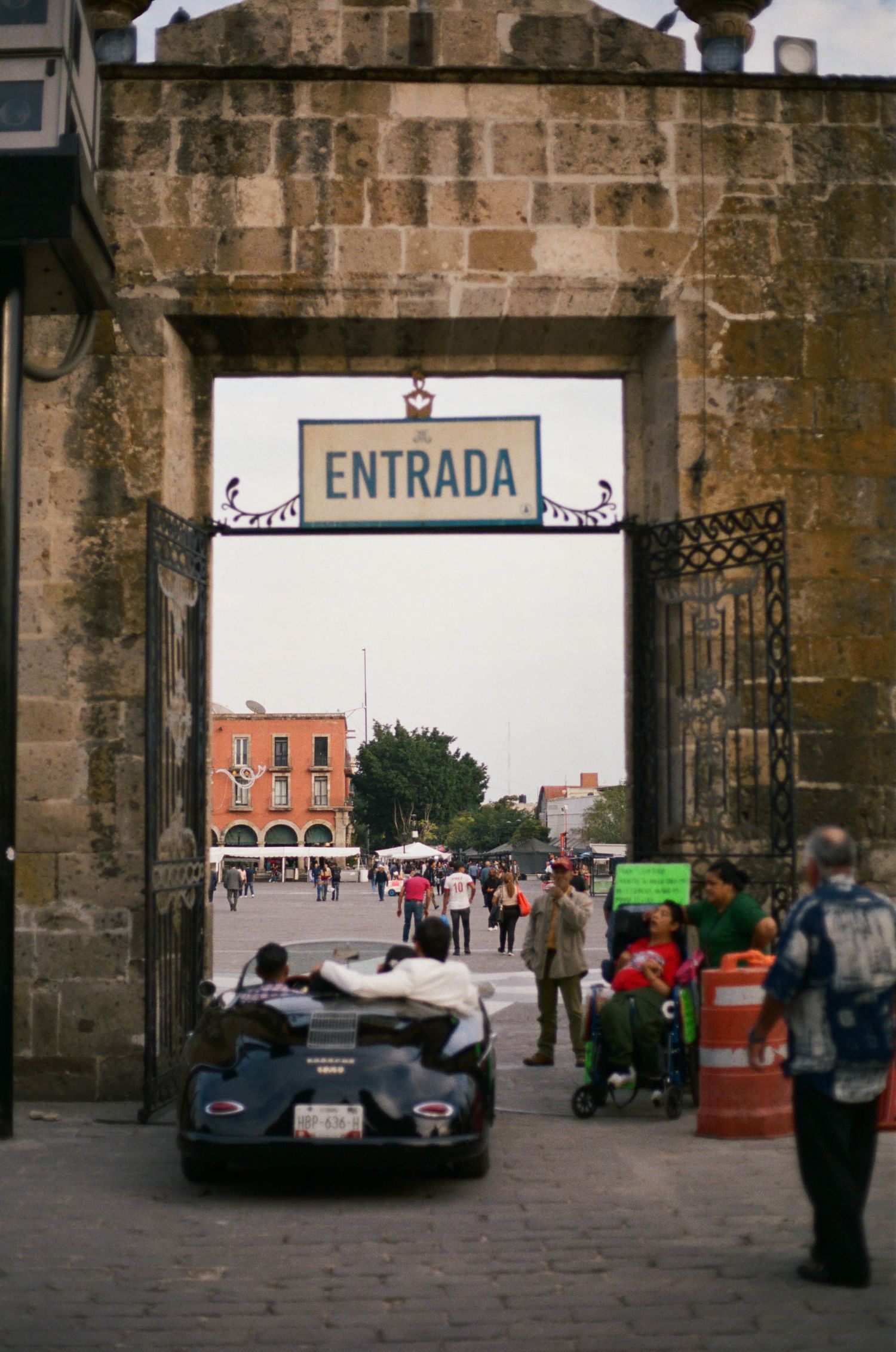 Stone archway entrance to historic venue with vintage cars and wedding guests visible.