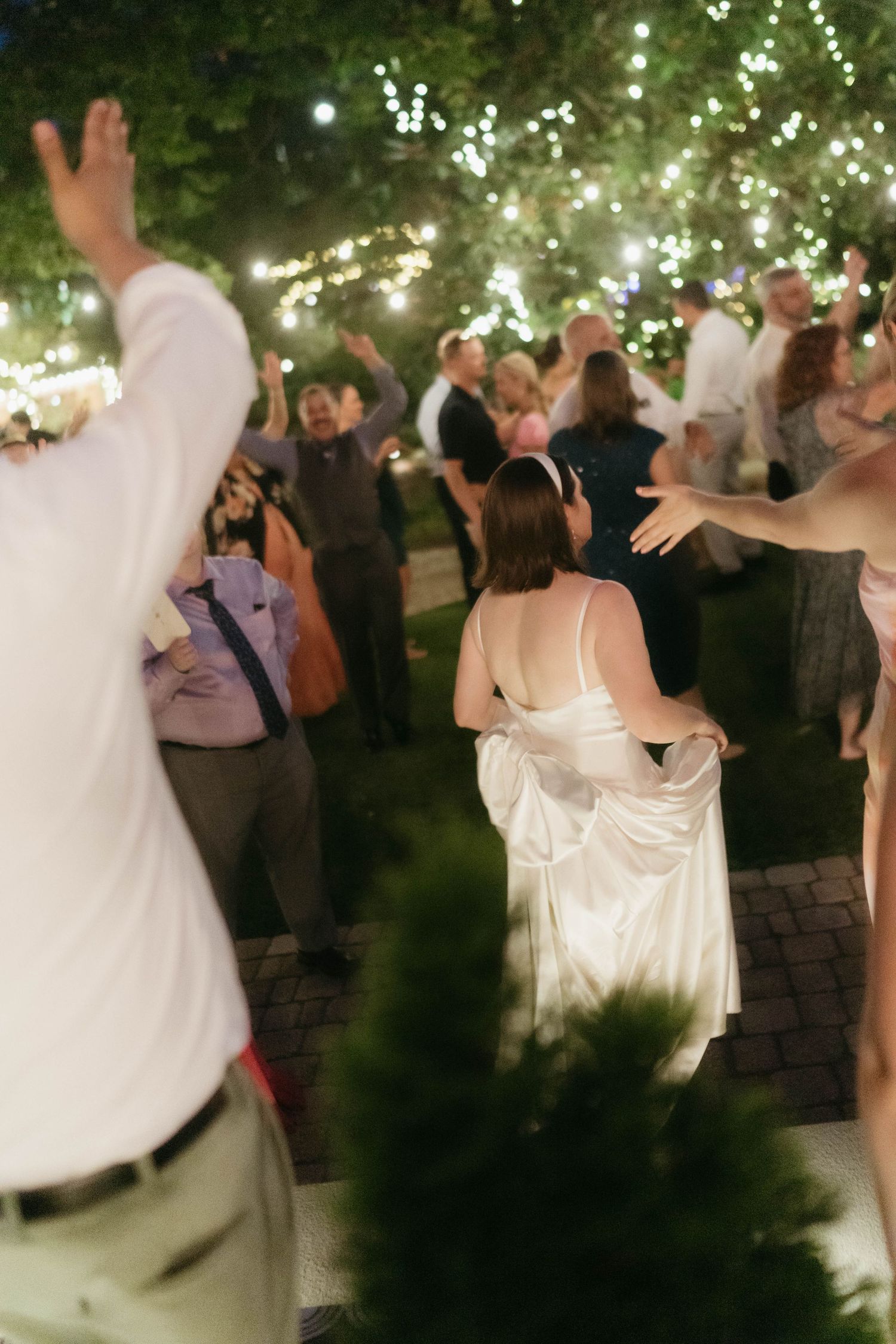 Couples dancing beneath glowing string lights at an outdoor evening celebration.