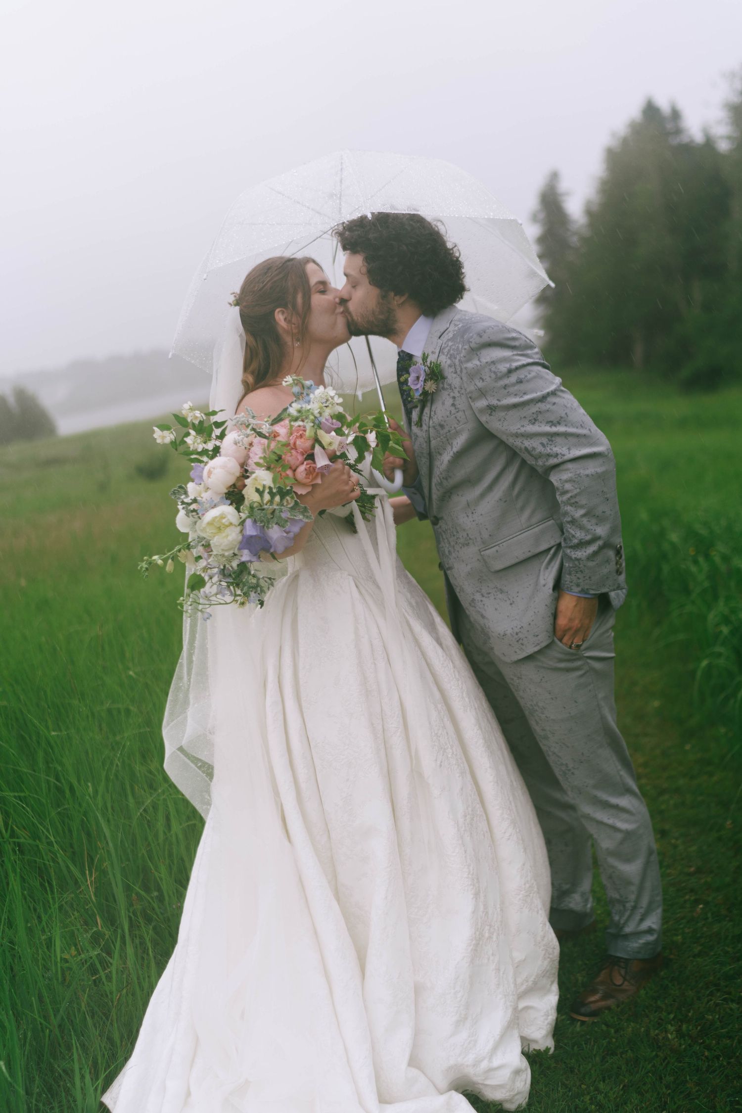 Romantic wedding moment captured in a misty field with flowing white dress and grey suit.