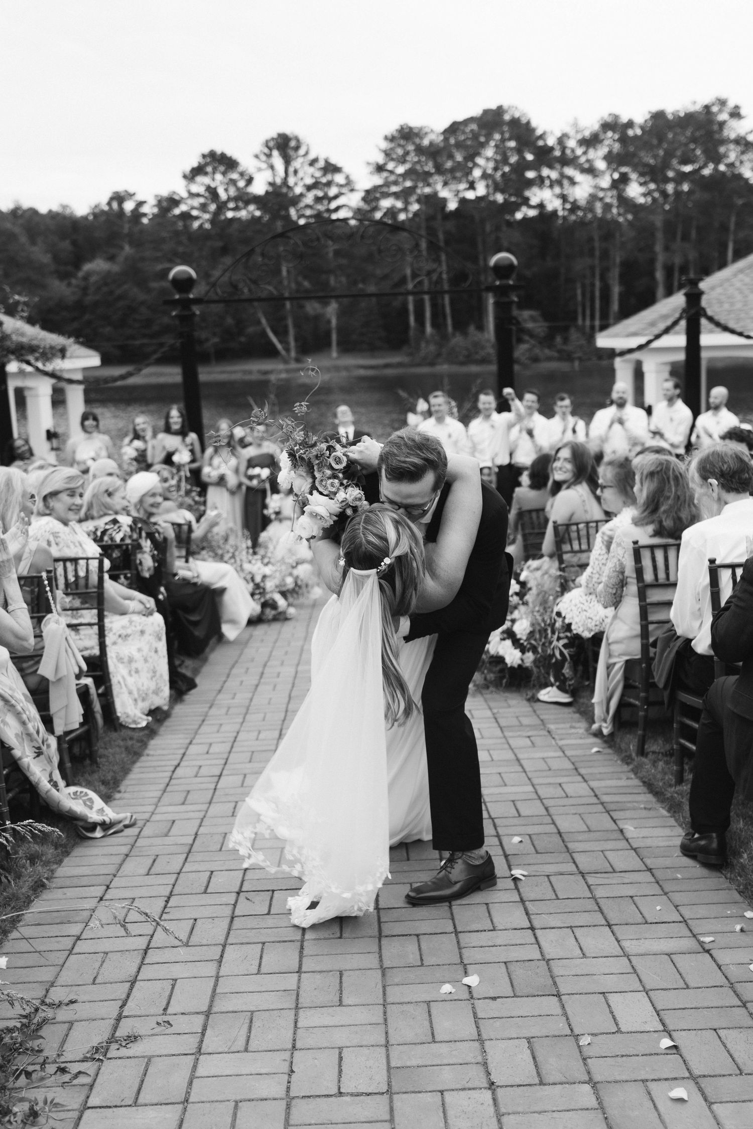 Black and white photo of groom dipping bride for a kiss while walking down the ceremony aisle.