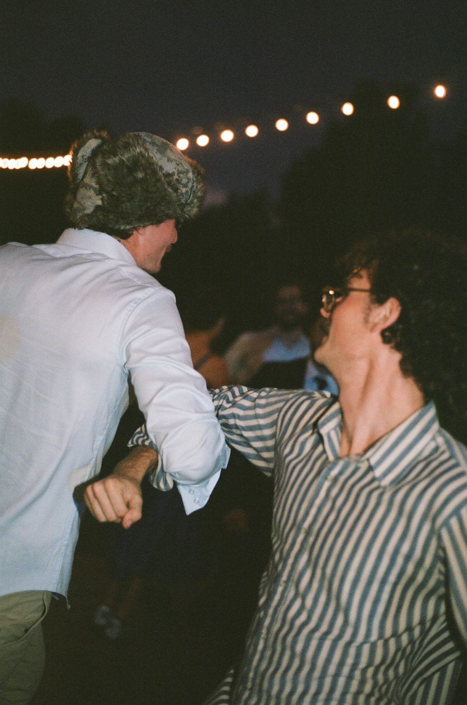 Two guests dance together at an outdoor evening wedding reception under string lights.