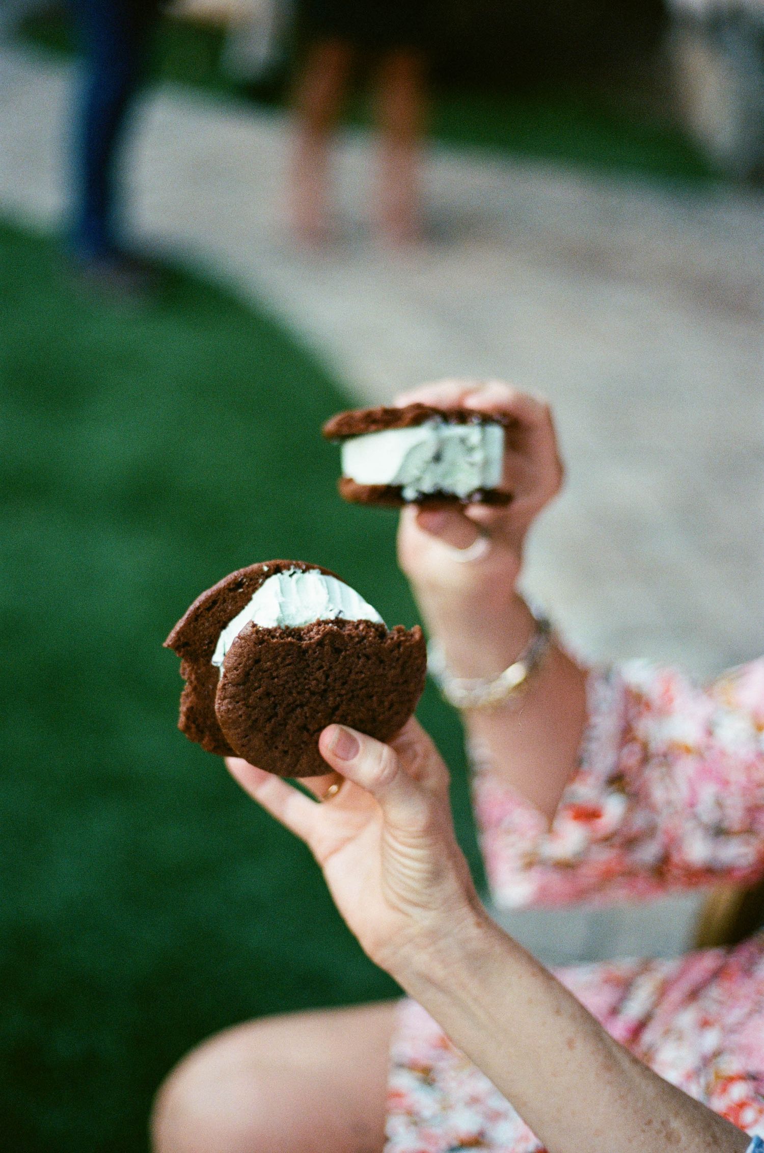 Hands holding chocolate whoopie pies with cream filling at an outdoor event.