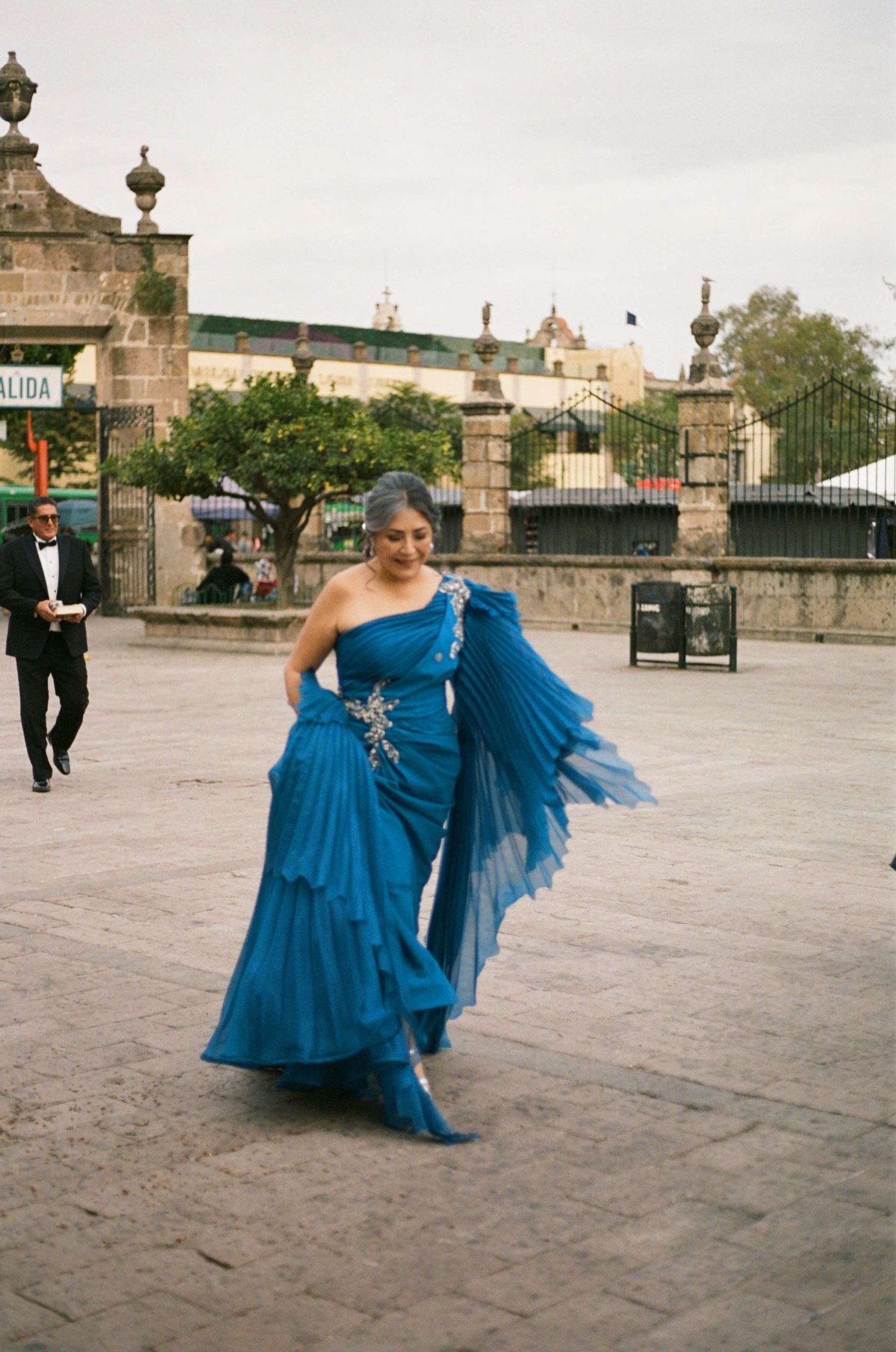 Person in a flowing blue evening gown poses in front of colonial architecture.