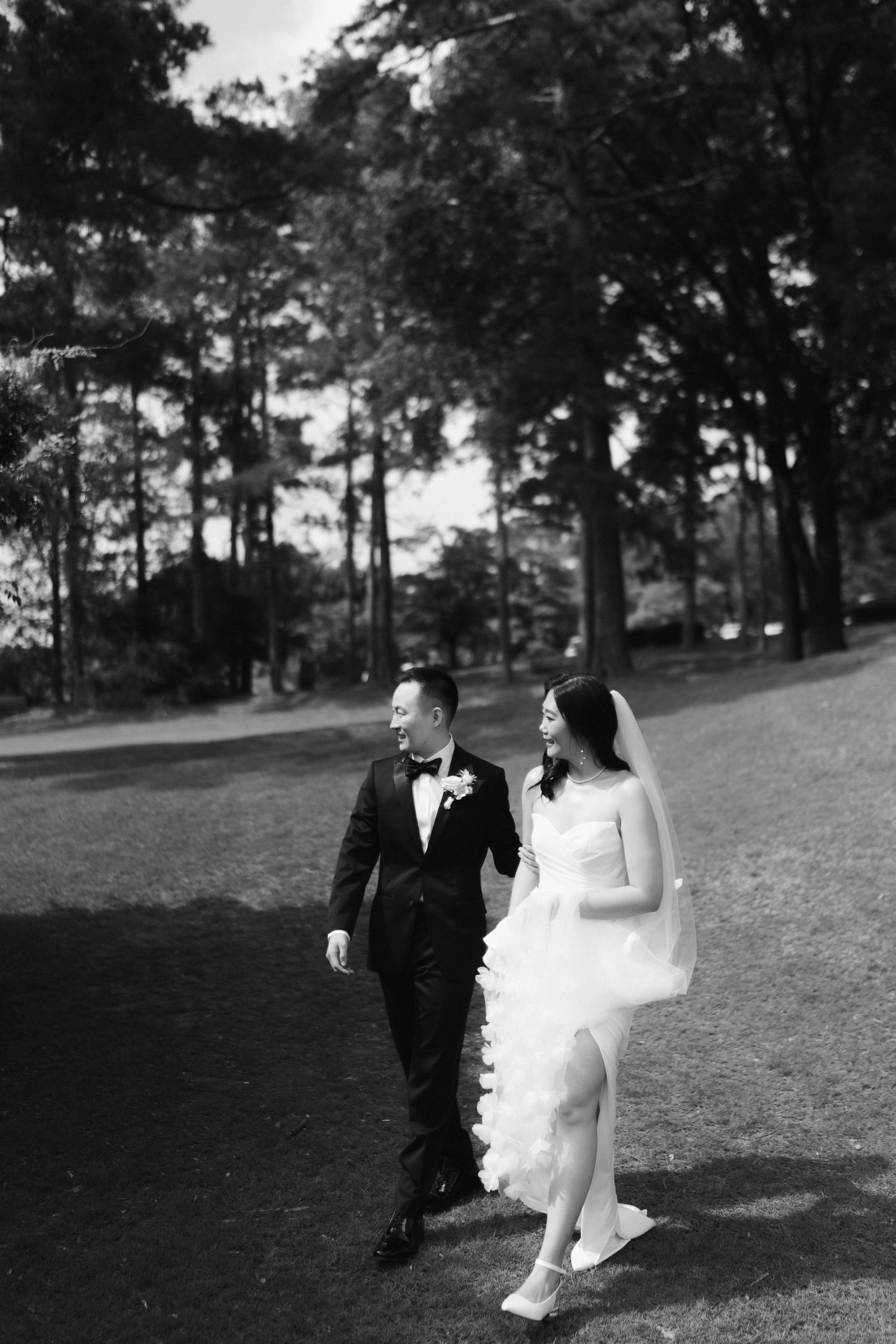 Wedding couple walks across a grassy hillside in black and white photography.