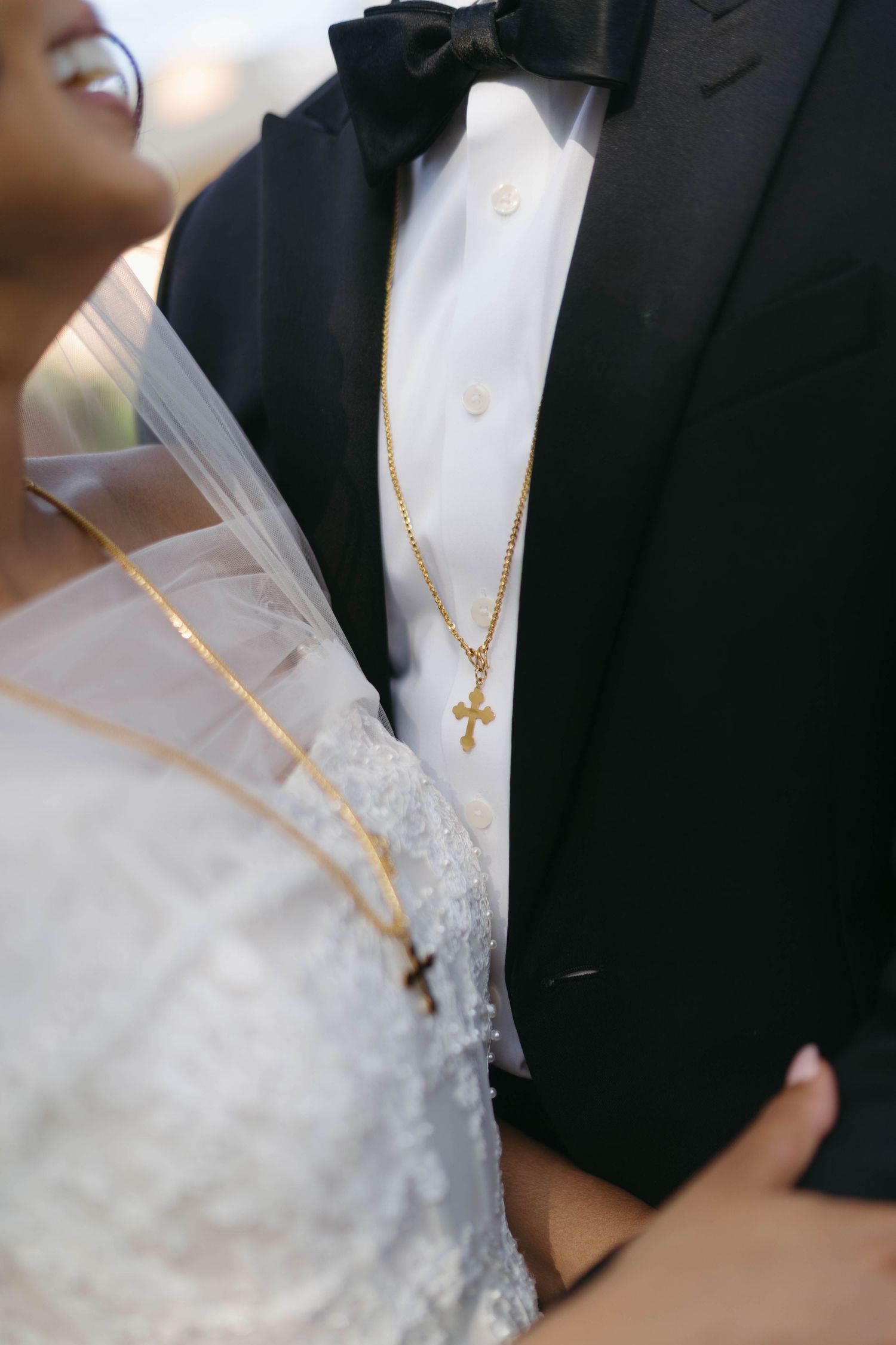 Close-up of bride and groom wearing matching gold cross necklaces at wedding ceremony.
