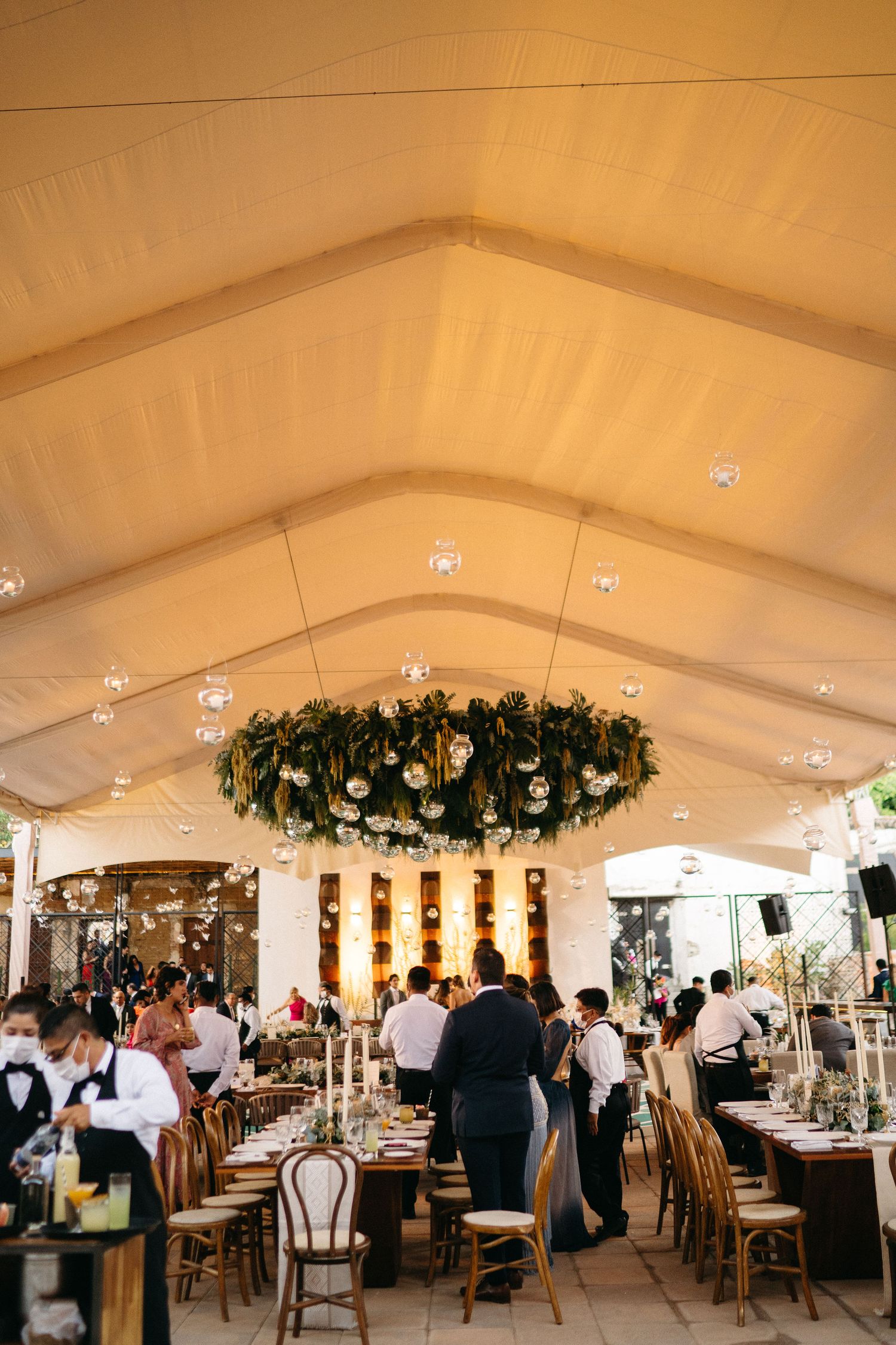 Elegant wedding reception setup under white tent with floral chandelier and formal table settings.