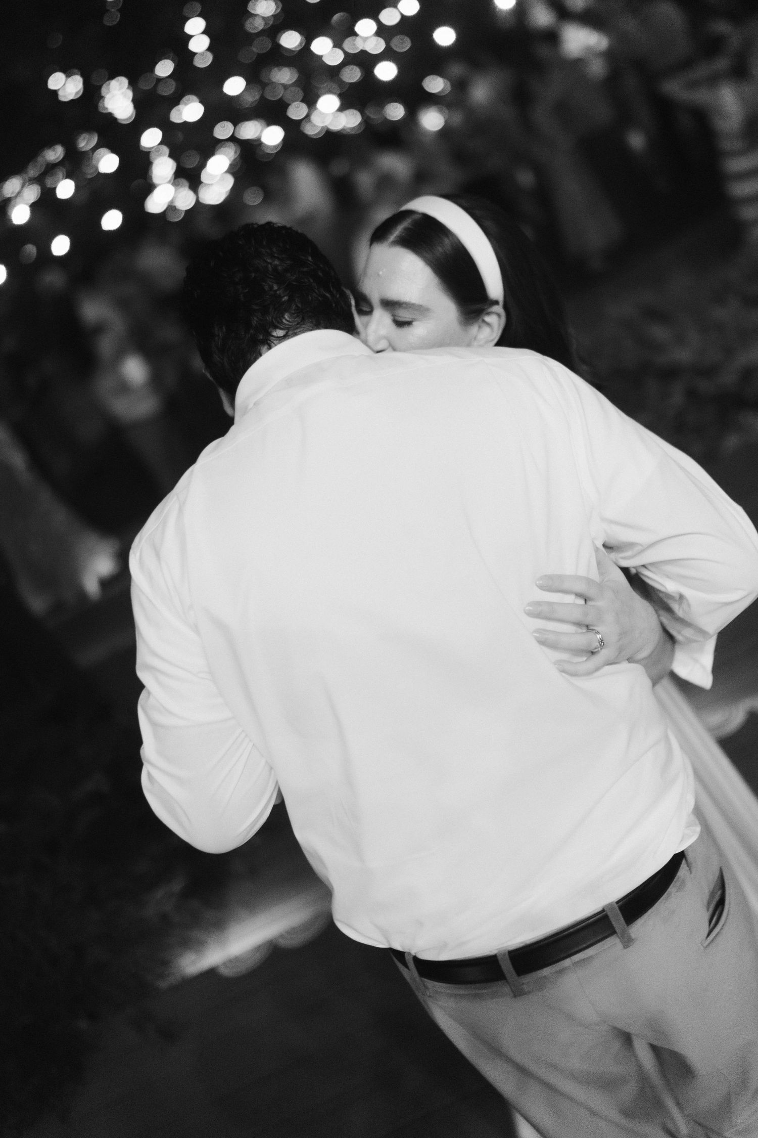 Black and white photo capturing an intimate dance moment under twinkling lights.