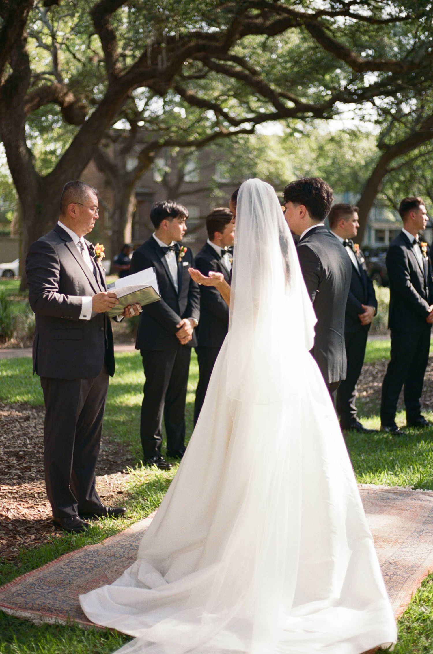 Wedding party stands in formation on a brick pathway surrounded by lush greenery.