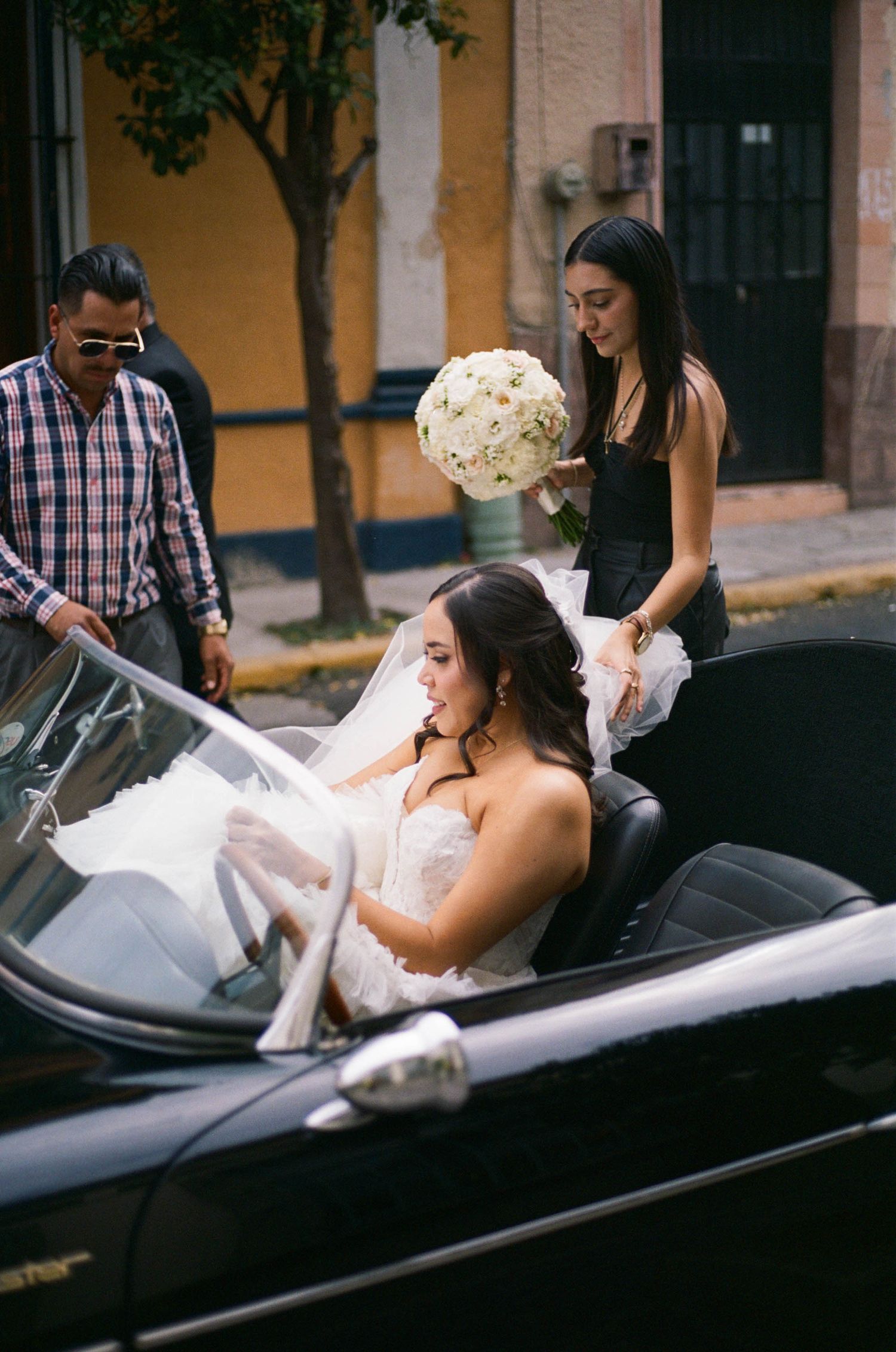 Wedding party helping with a white dress in a vintage black car.