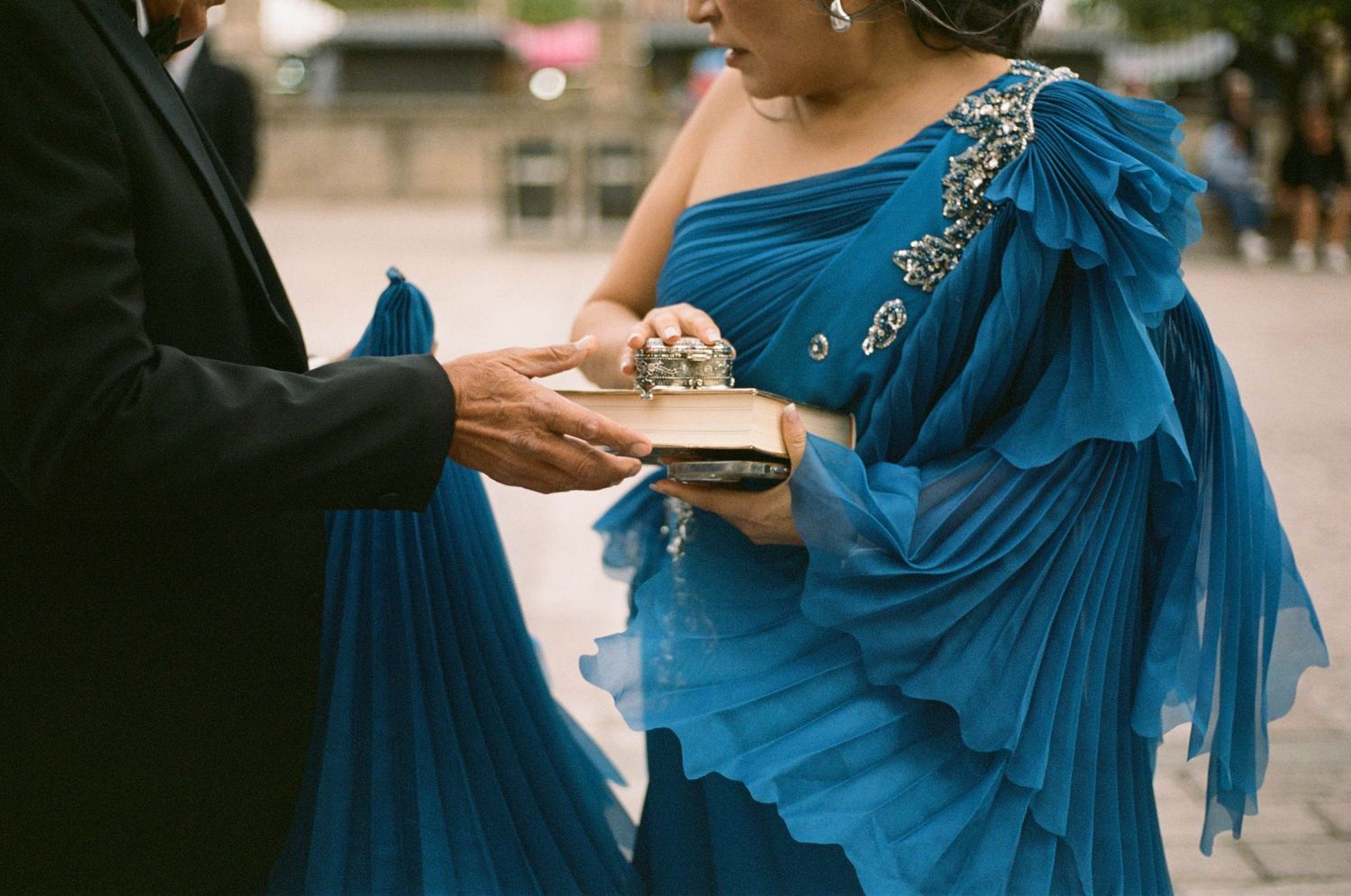 A woman in an elegant blue evening gown with ruffled details walks outdoors at a formal event.