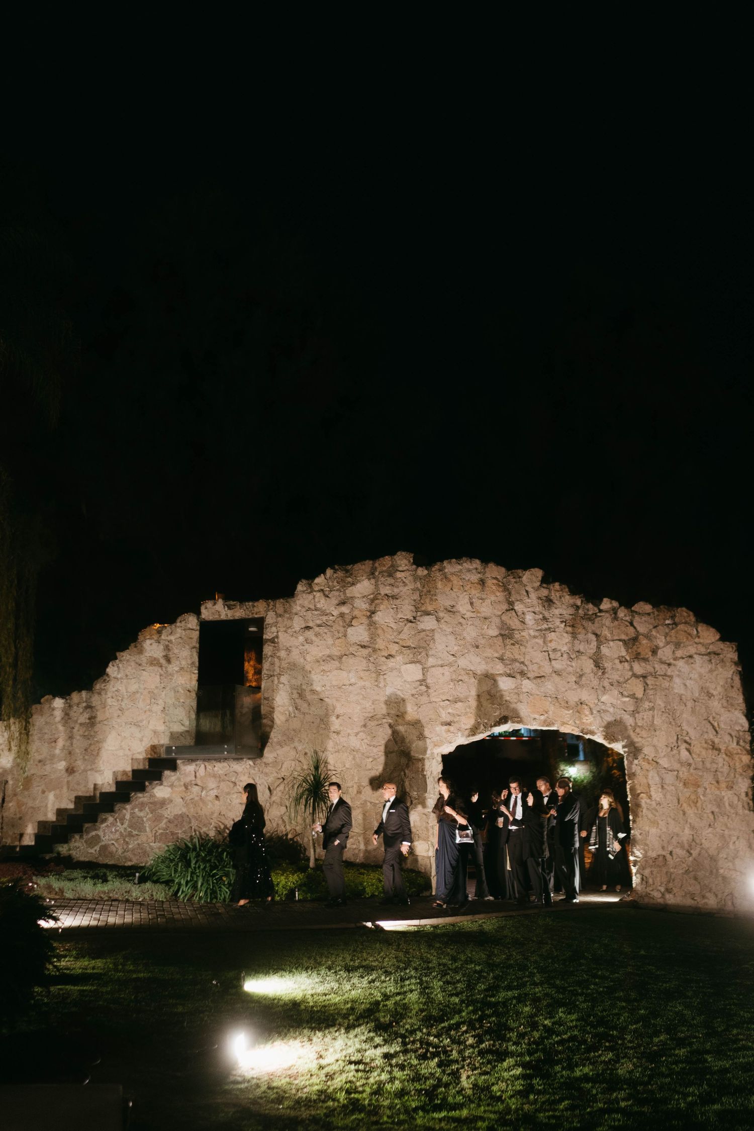 Ancient stone ruins illuminated at night with visitors exploring the historic site under spotlights.