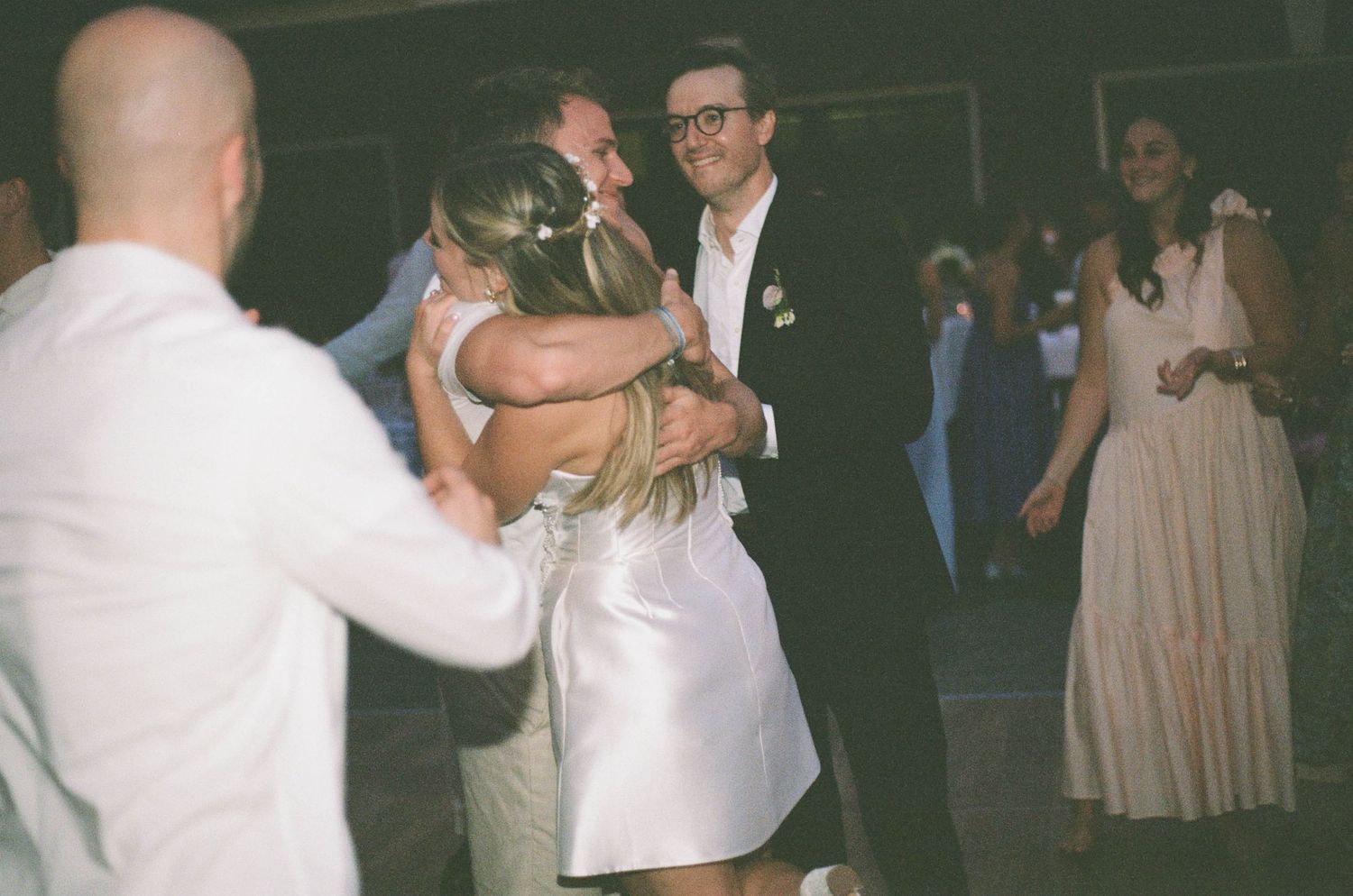Bride and groom share a warm embrace with guests on the wedding reception dance floor.