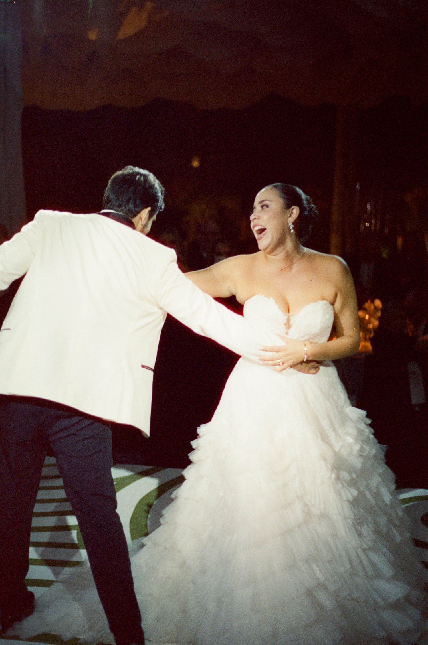 Newlyweds share their first dance in an elegant ballroom with the bride wearing a layered tulle gown.