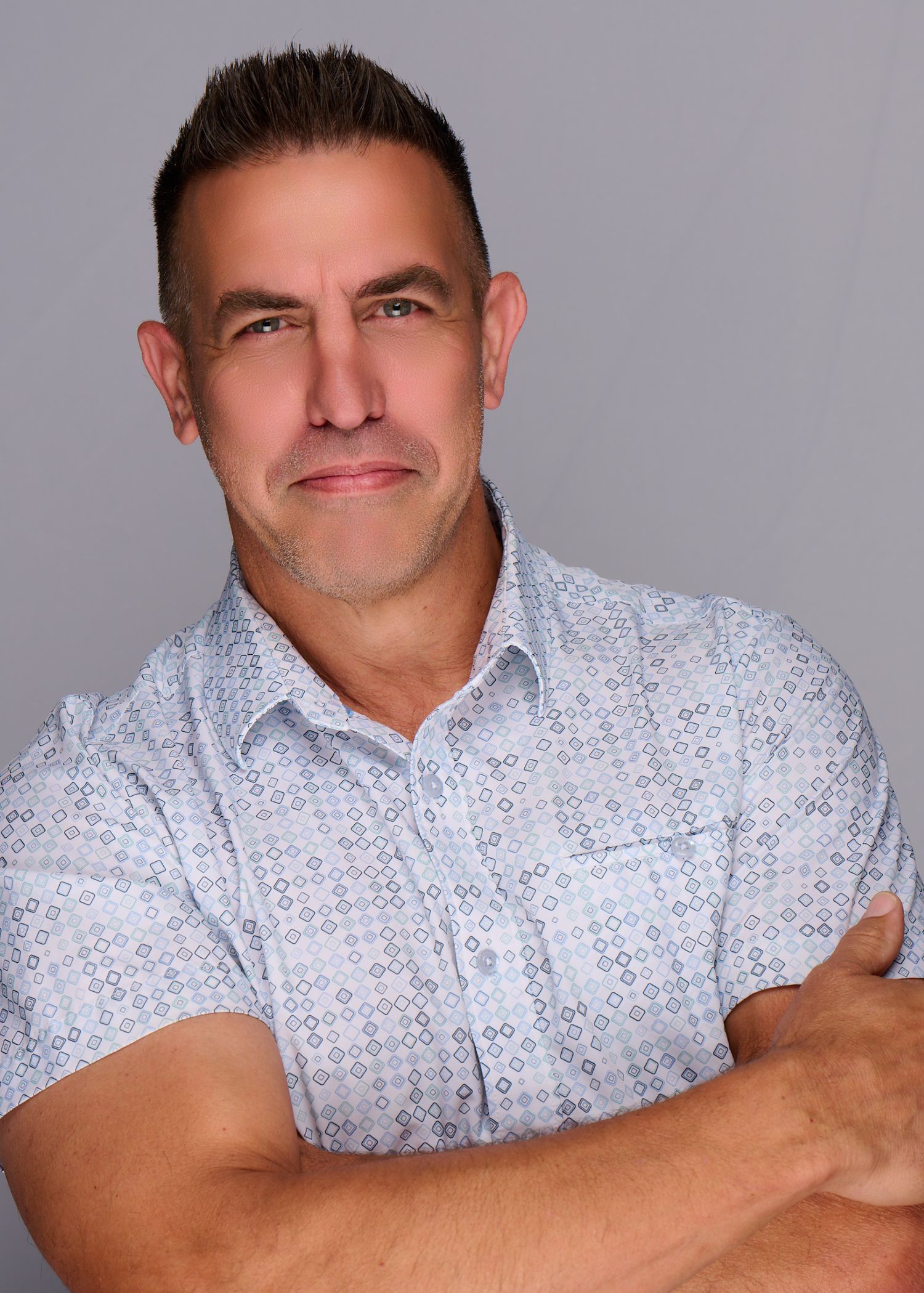 Professional portraits of person in patterned short-sleeve shirt against gray background.