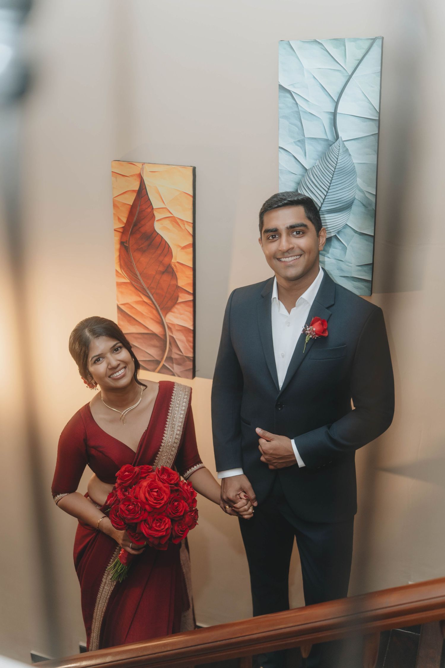 Candid wedding moment, couple smiling with red bouquet in warmly lit room