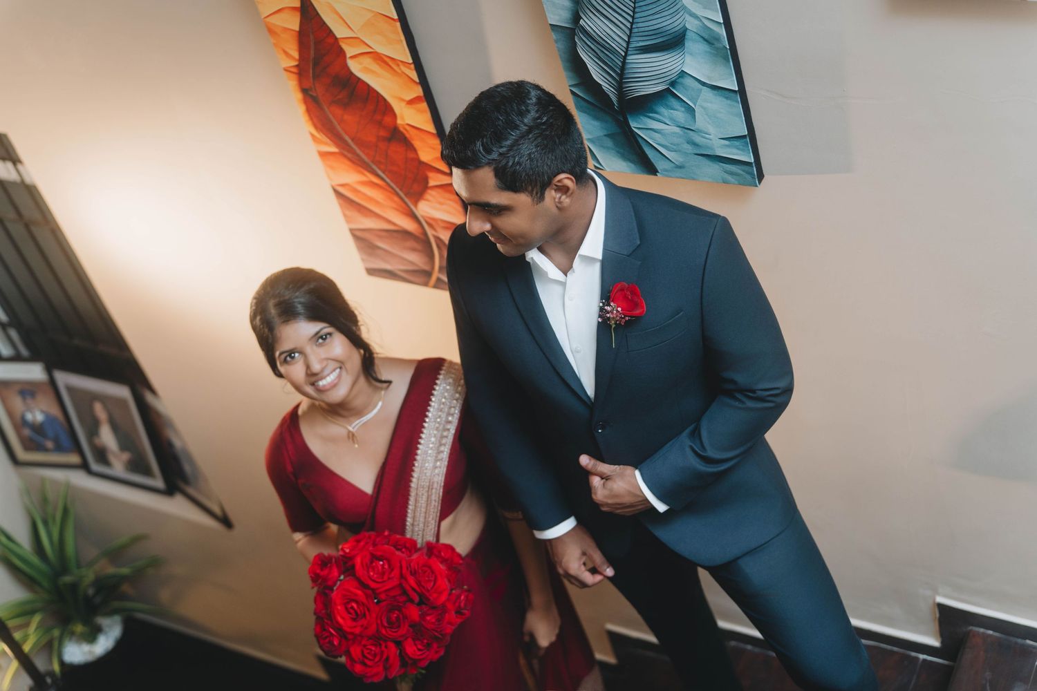 Candid wedding moment, couple smiling with red bouquet in warmly lit room