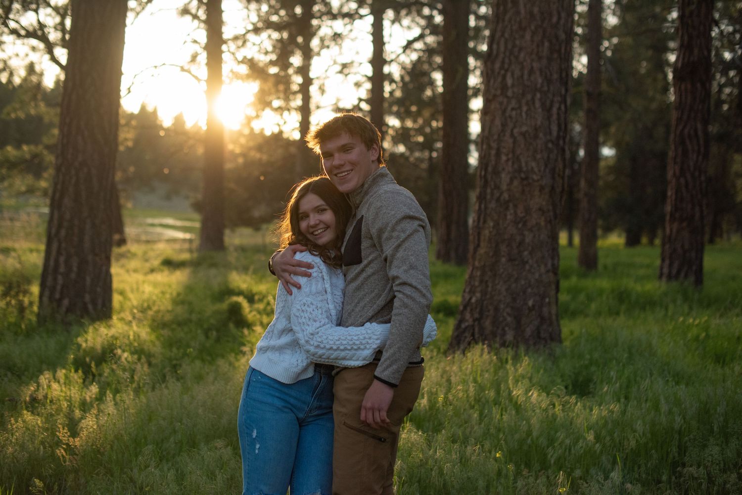 Happy couple hugging and smiling in a sunlit pine forest with golden hour light.