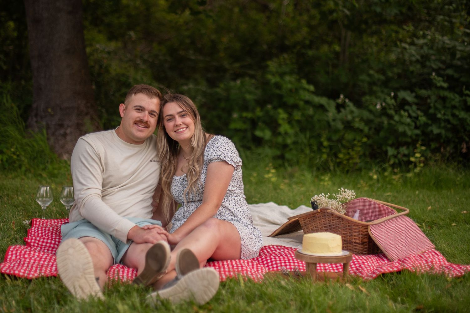 Smiling couple relaxing together on a red checkered blanket during a sunny outdoor picnic in the park.