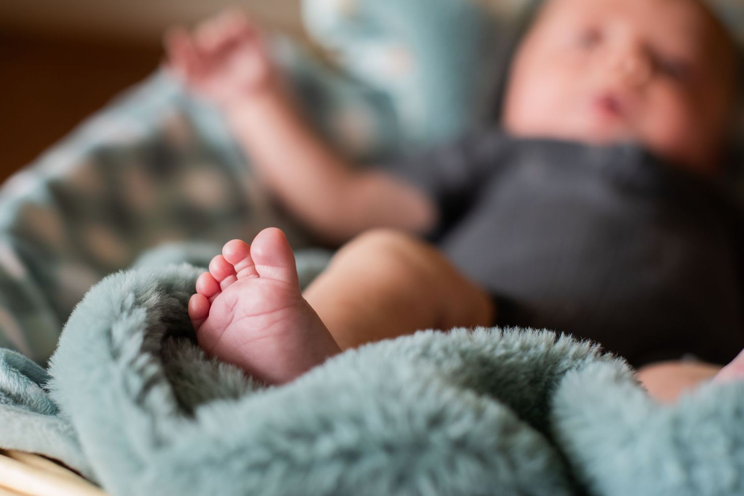 Close-up of a newborn babys tiny foot resting on a soft teal blanket in a wicker basket.
