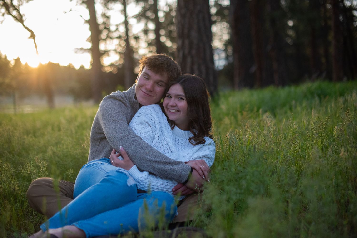 Couple sitting and cuddling in a lush meadow with warm golden sunset light behind them.