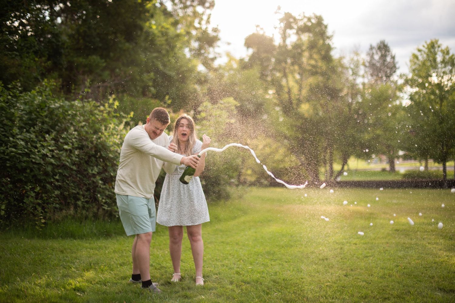 Couple joyfully popping a confetti popper together in a lush green garden during golden hour.