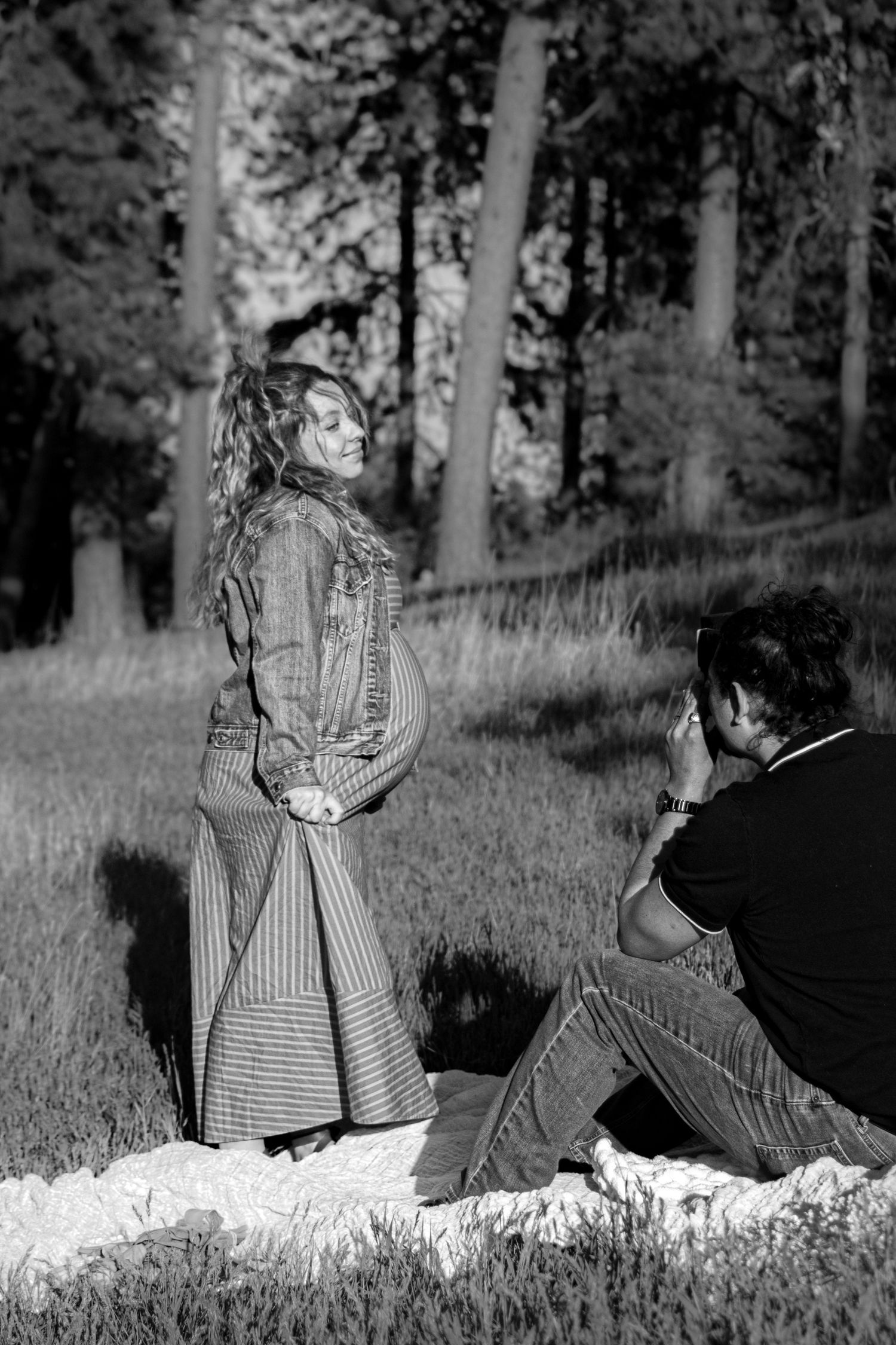 Black and white photo of a woman posing in a field while a photographer captures her portrait outdoors.