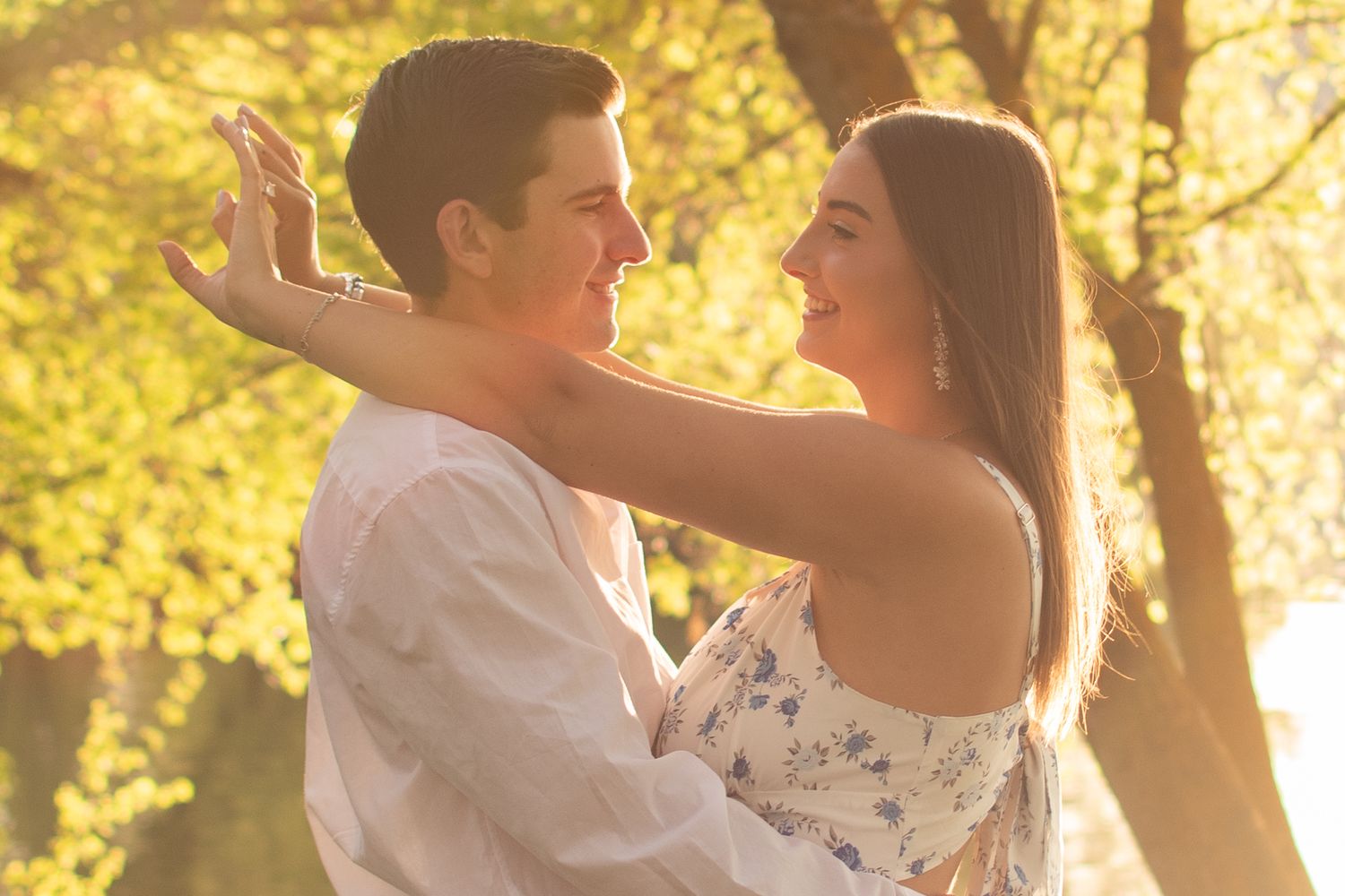 Young couple embracing and smiling at each other in a sunlit park with golden trees in the background.