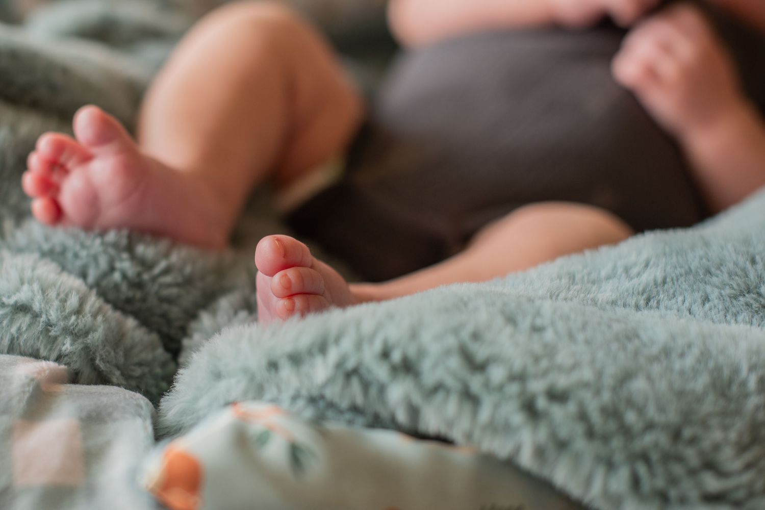 Newborn baby feet resting on a soft teal and patterned blanket during a newborn photo session.