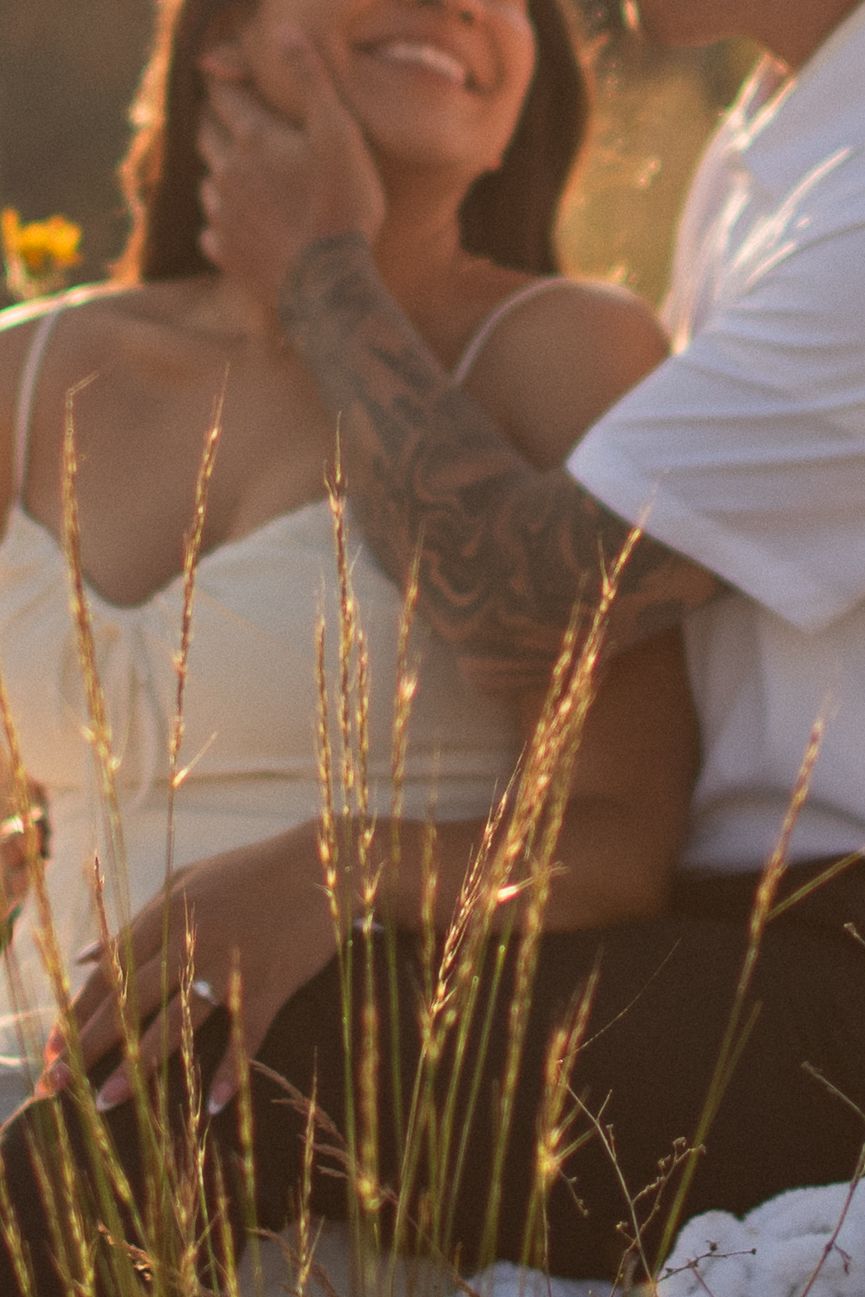 Couple sharing a romantic moment in golden sunlight, man with tattooed arm gently touching womans face as she smiles.