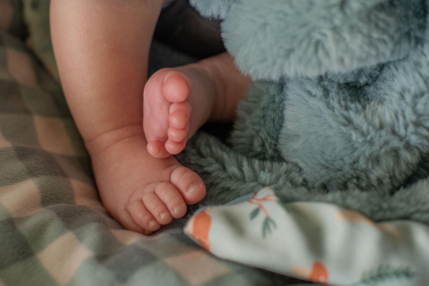 Adorable newborn baby feet resting on a soft green textured blanket with floral accents.