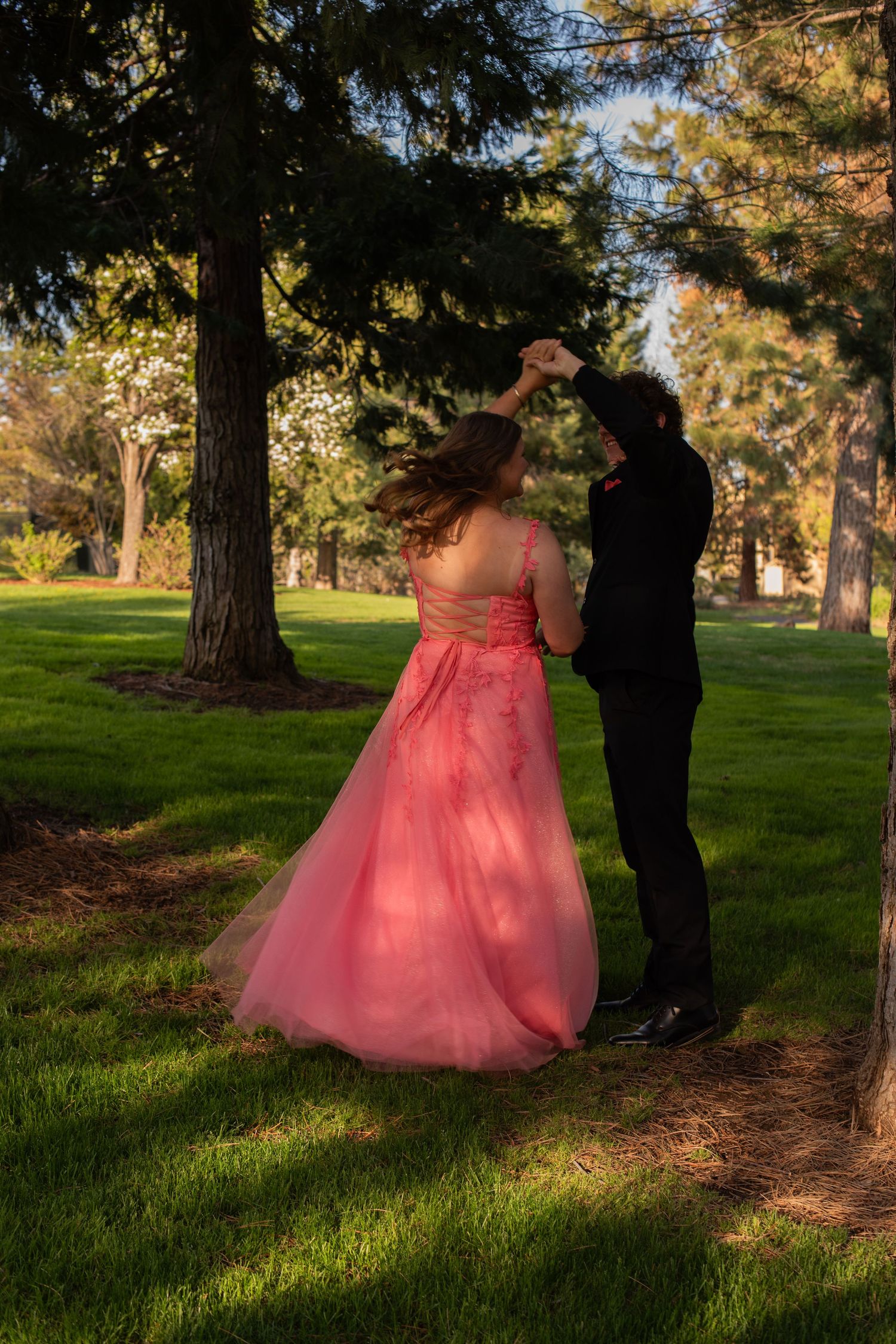 Couple dancing outdoors in a park, woman in pink ball gown being twirled by man in black suit.