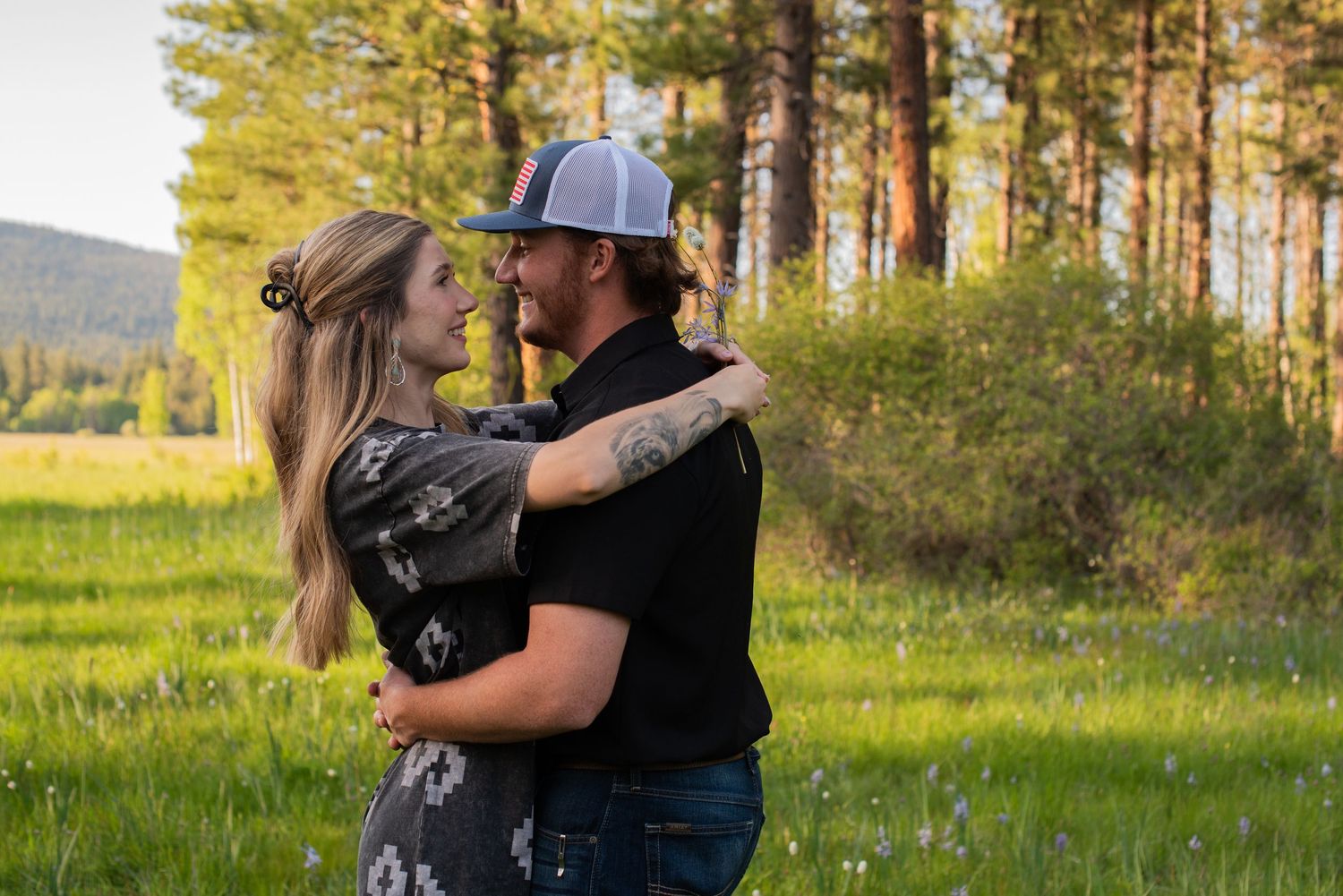 Couple embracing and gazing at each other in a scenic mountain meadow.