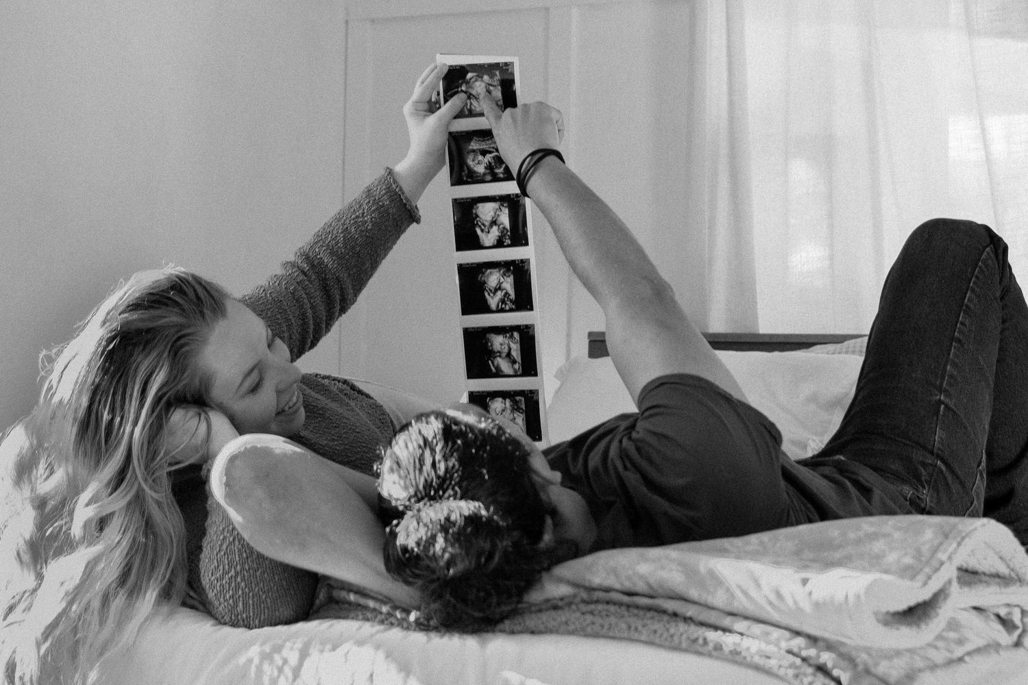 Couple lying on bed in black and white photo looking at ultrasound images together.