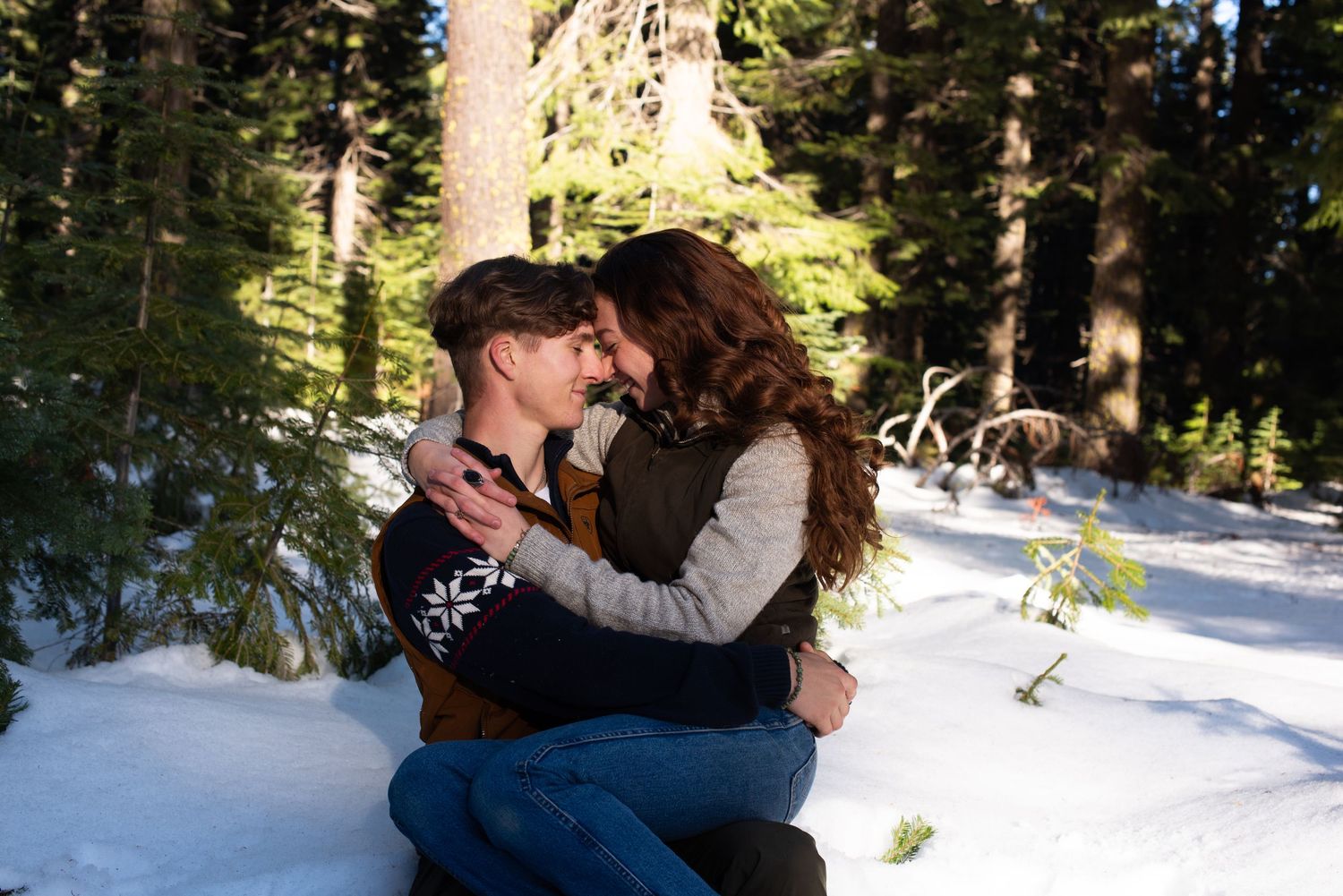Couple sharing a romantic moment in a snowy forest, surrounded by pine trees in winter.