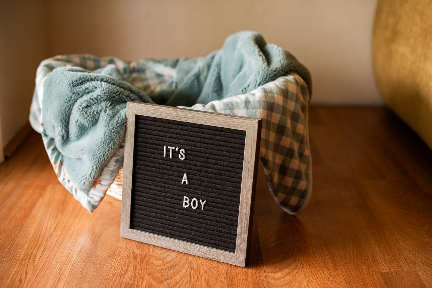 An Its A Boy letter board sign displayed in front of an empty wicker basket with blue blankets.