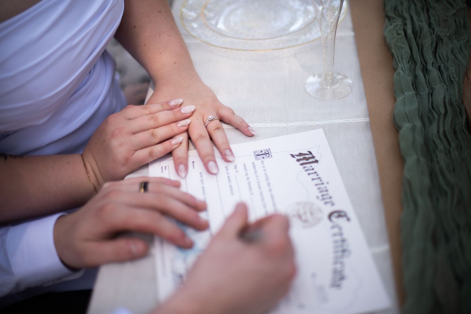 Bride and groom hands with wedding rings resting on a marriage certificate at their ceremony.