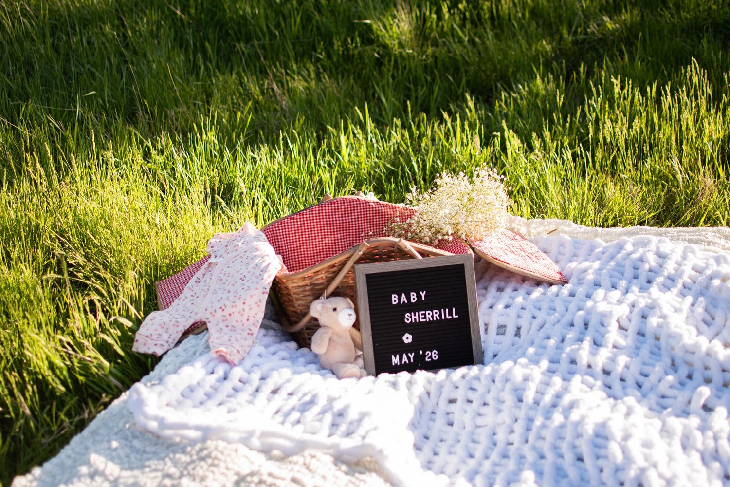 Baby announcement letter board reading Baby Sherrill May 26 on white blanket in grass.