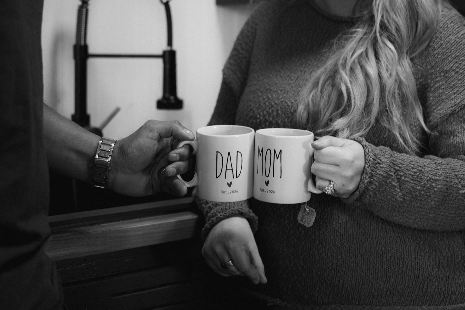 Black and white photo of couple holding Dad and Mom mugs, a heartfelt pregnancy announcement moment.