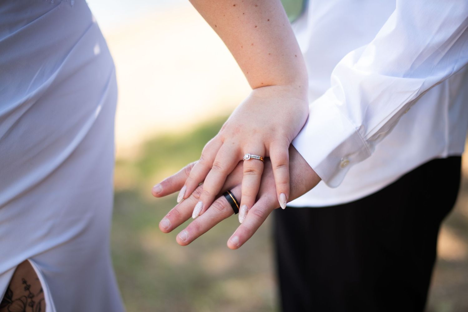 Close-up of newlyweds holding hands showing wedding bands in warm outdoor light.