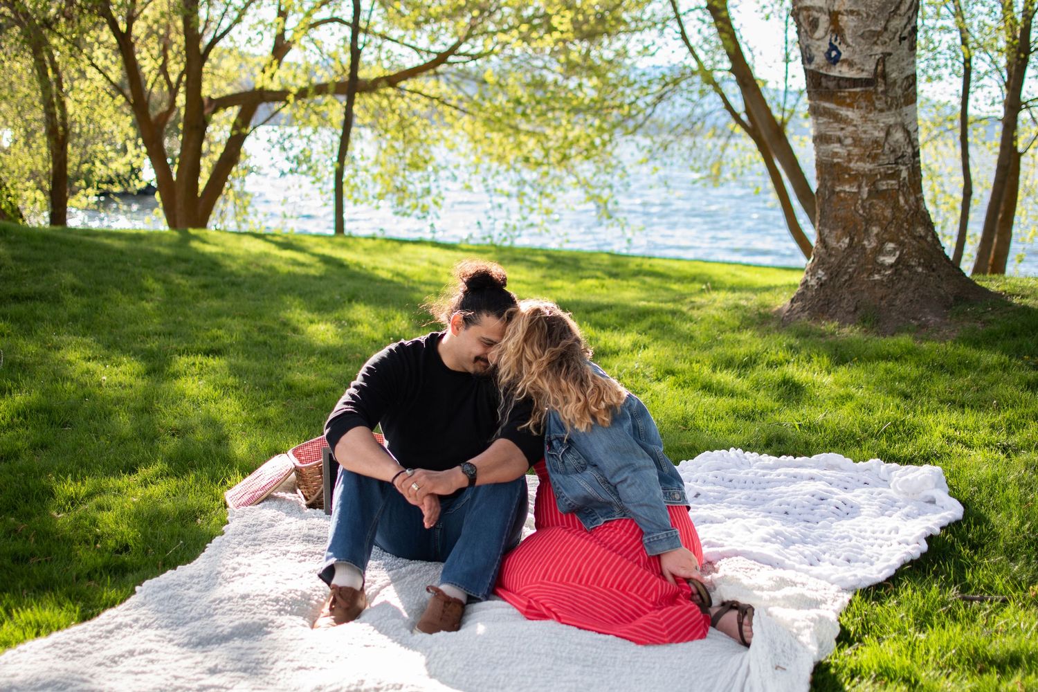 Couple sitting on a blanket by the lake sharing a tender moment.